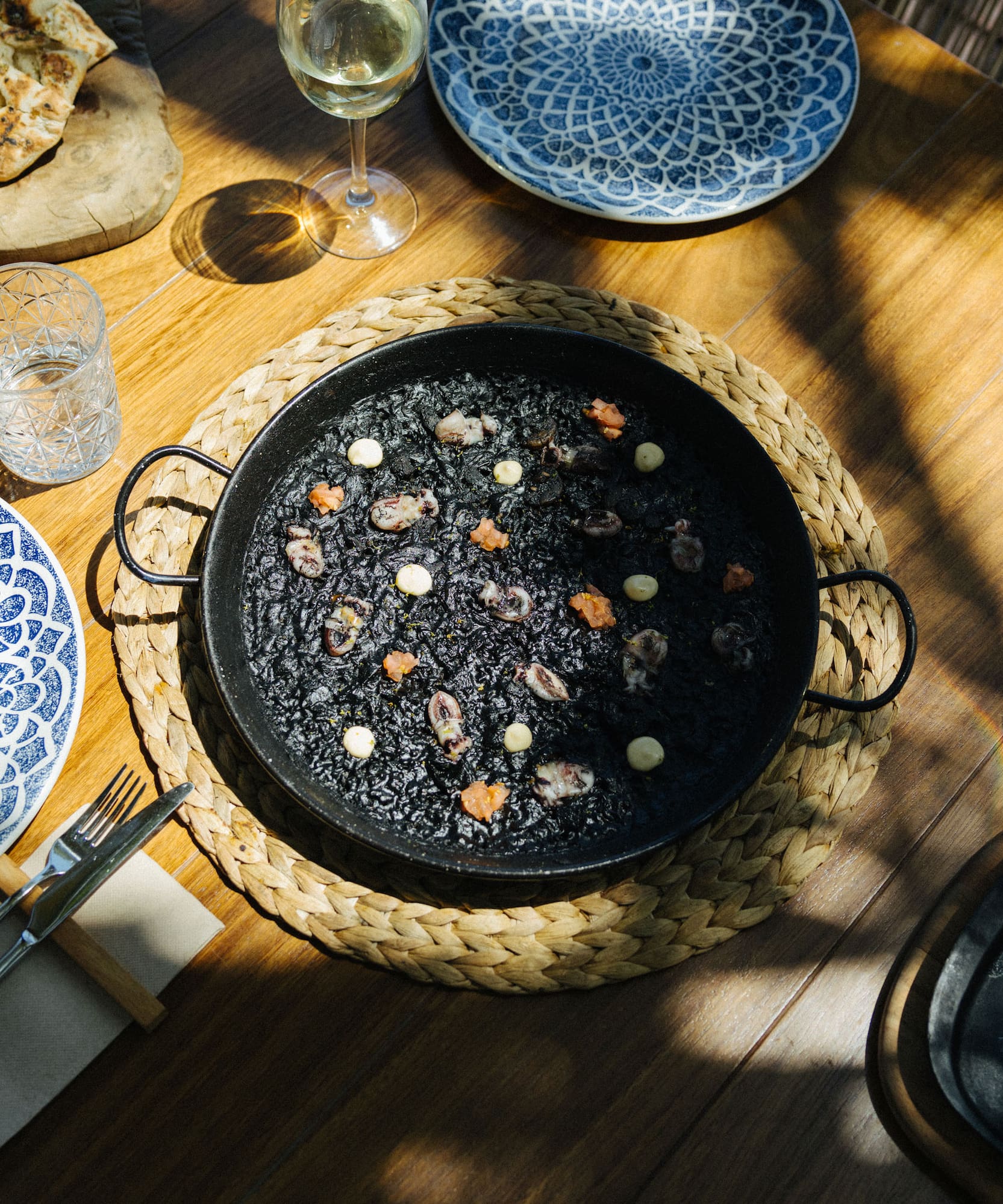 Arroz negro con mariscos, vino blanco y platos decorados en mesa de restaurante.