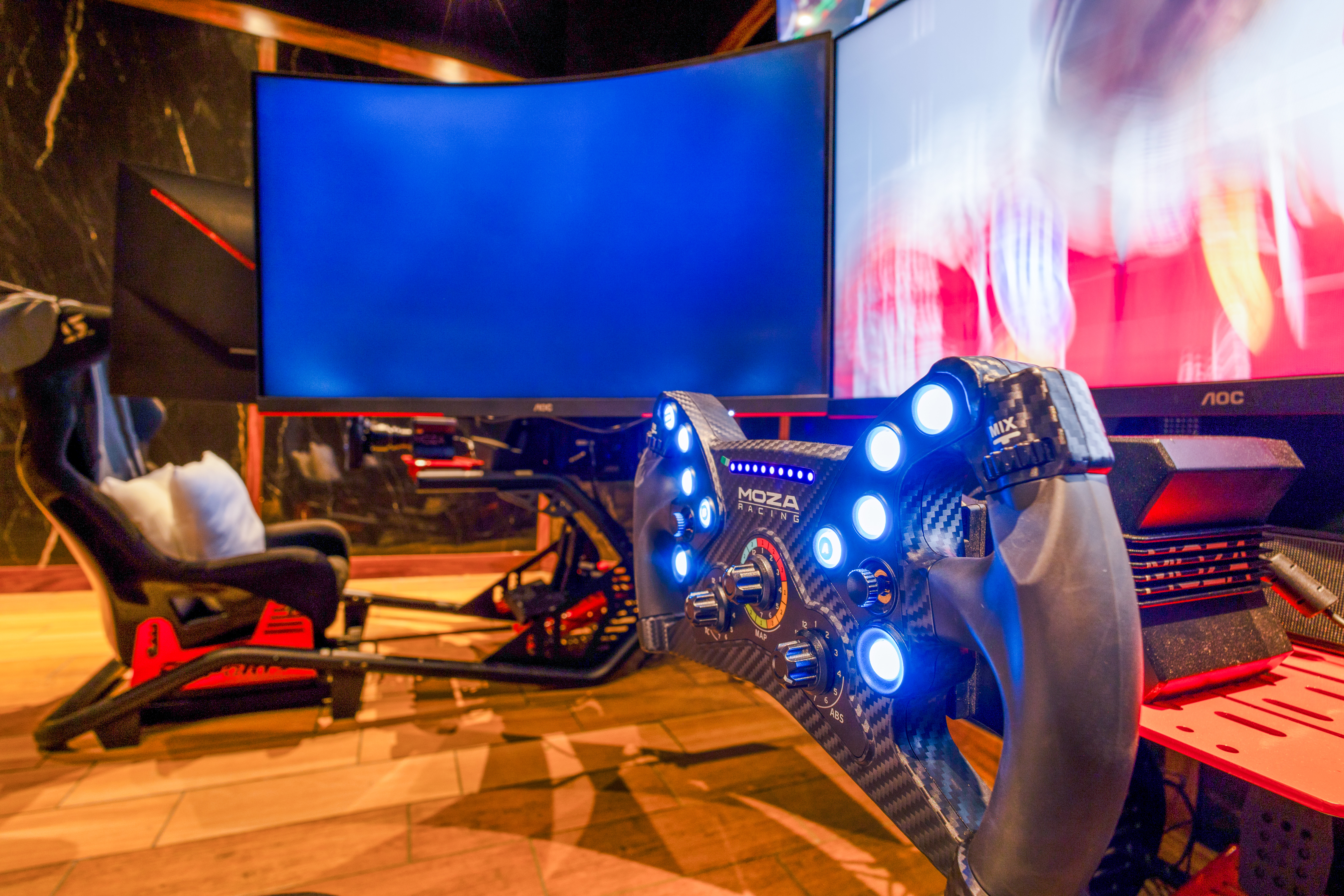 Moza Racing sim racing cockpit with illuminated wheel and gaming monitors.