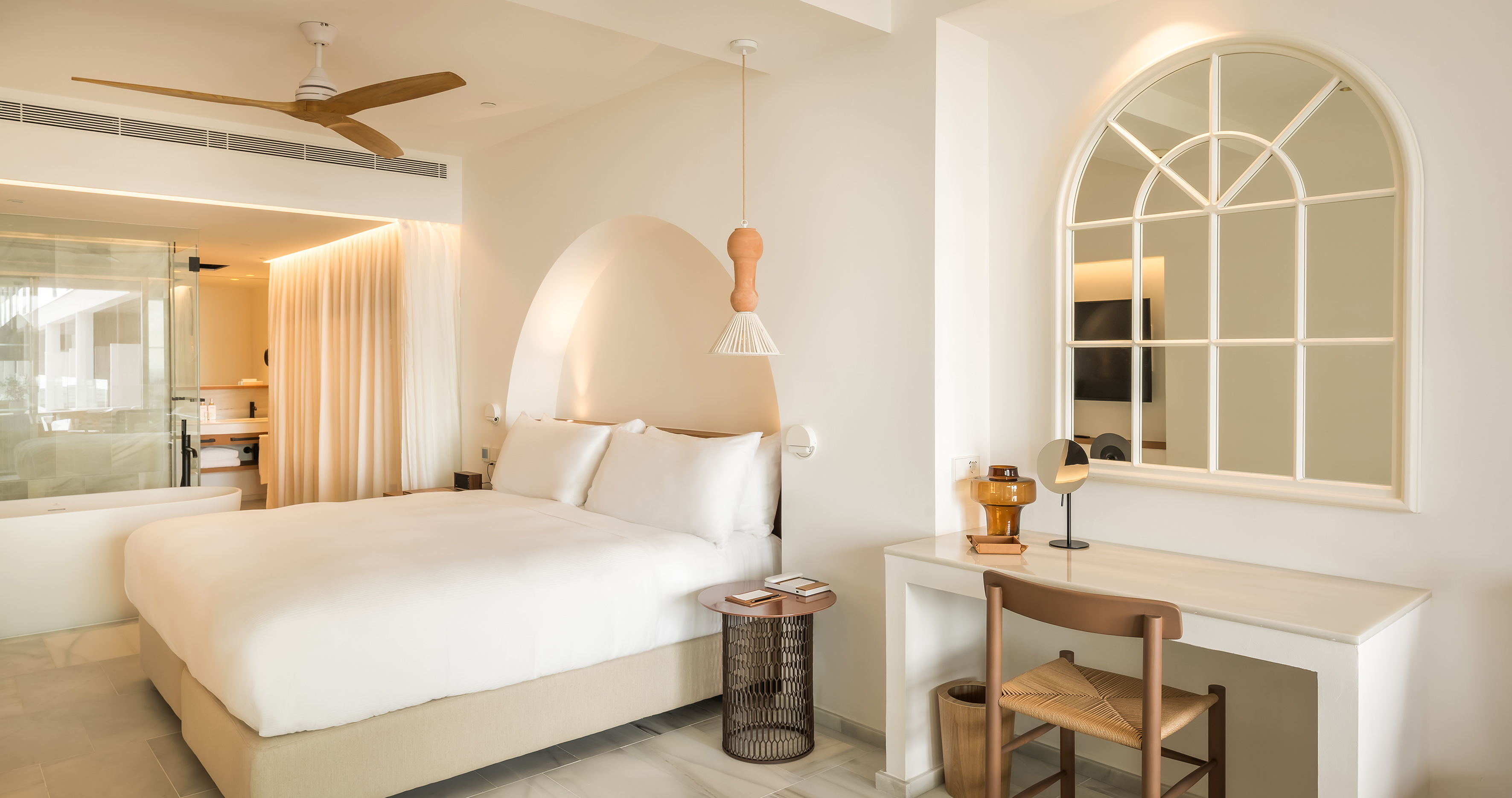 Modern white hotel bedroom with arched alcove, wooden fan, and integrated bathroom.