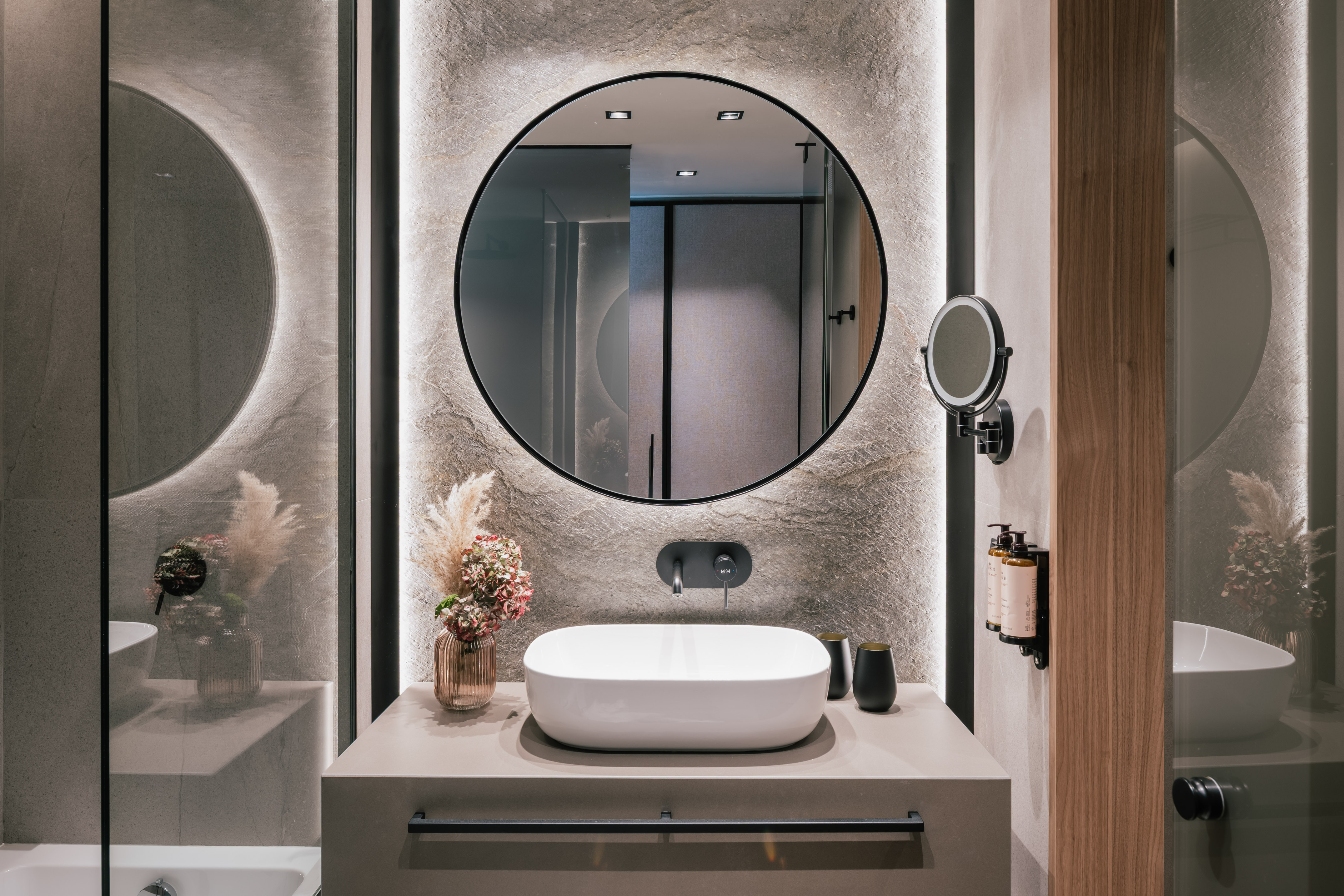 Modern bathroom vanity with round backlit mirror, white vessel sink, and concrete wall.