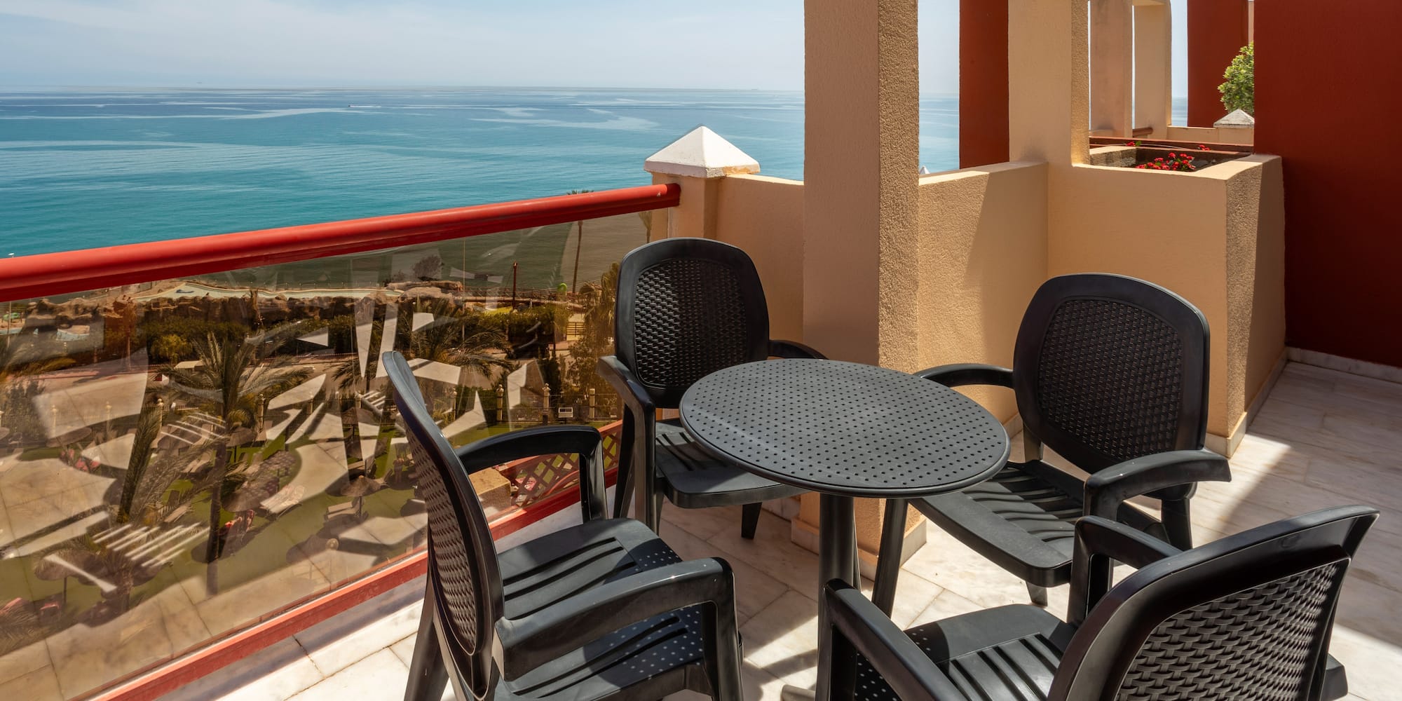 Sunny balcony with dark patio furniture and wide blue ocean view.