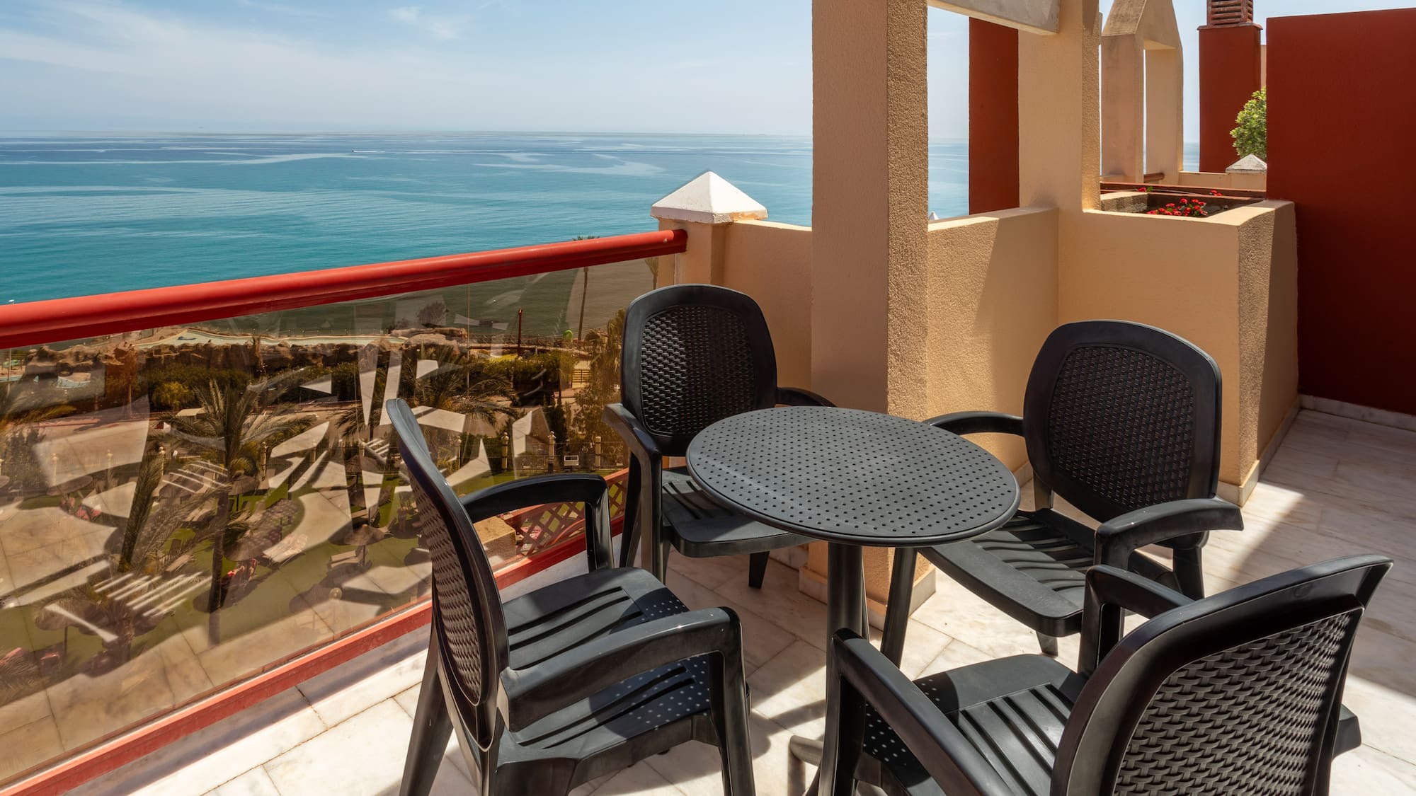 Sunny balcony with dark patio furniture and wide blue ocean view.