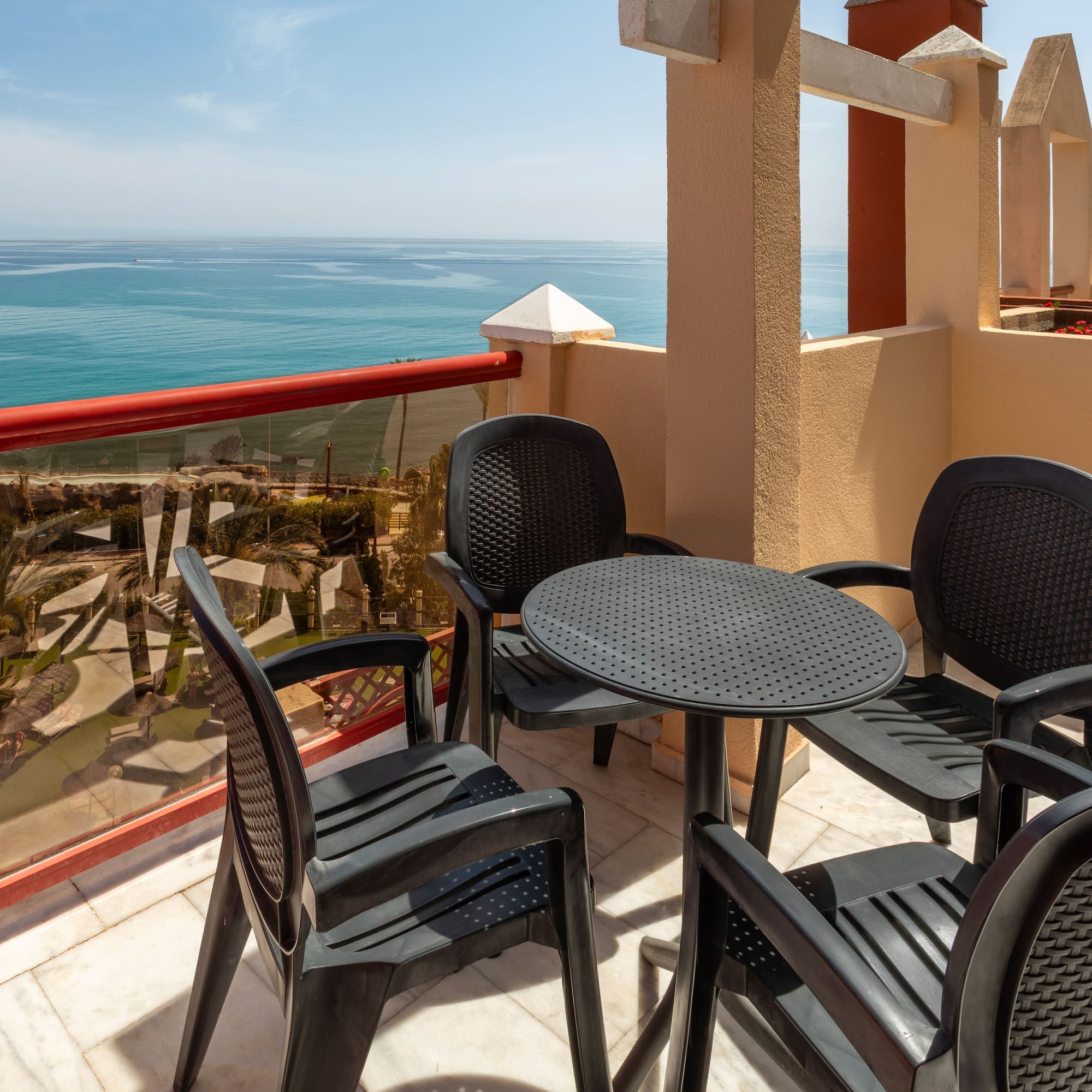 Sunny balcony with dark patio furniture and wide blue ocean view.