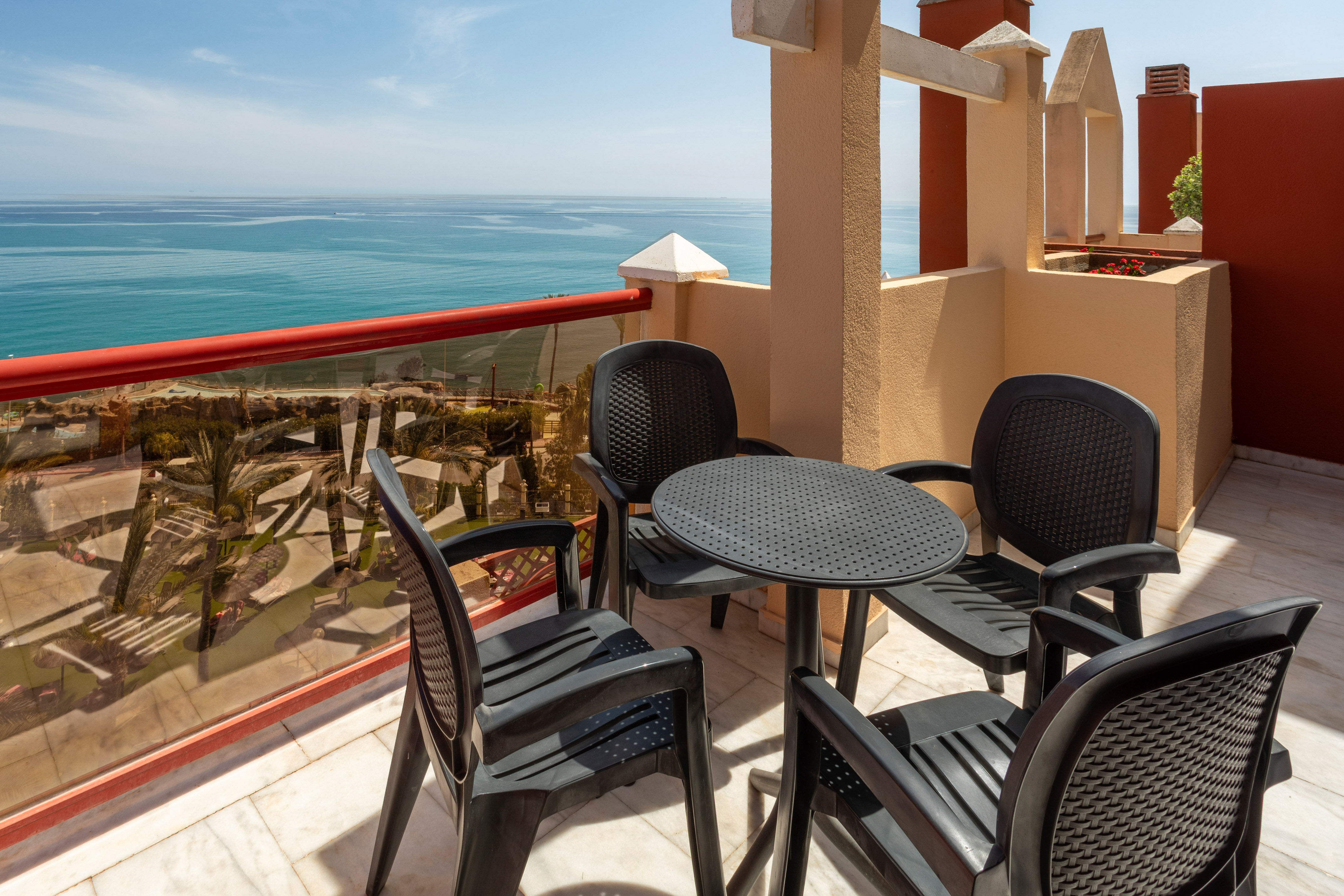 Sunny balcony with dark patio furniture and wide blue ocean view.