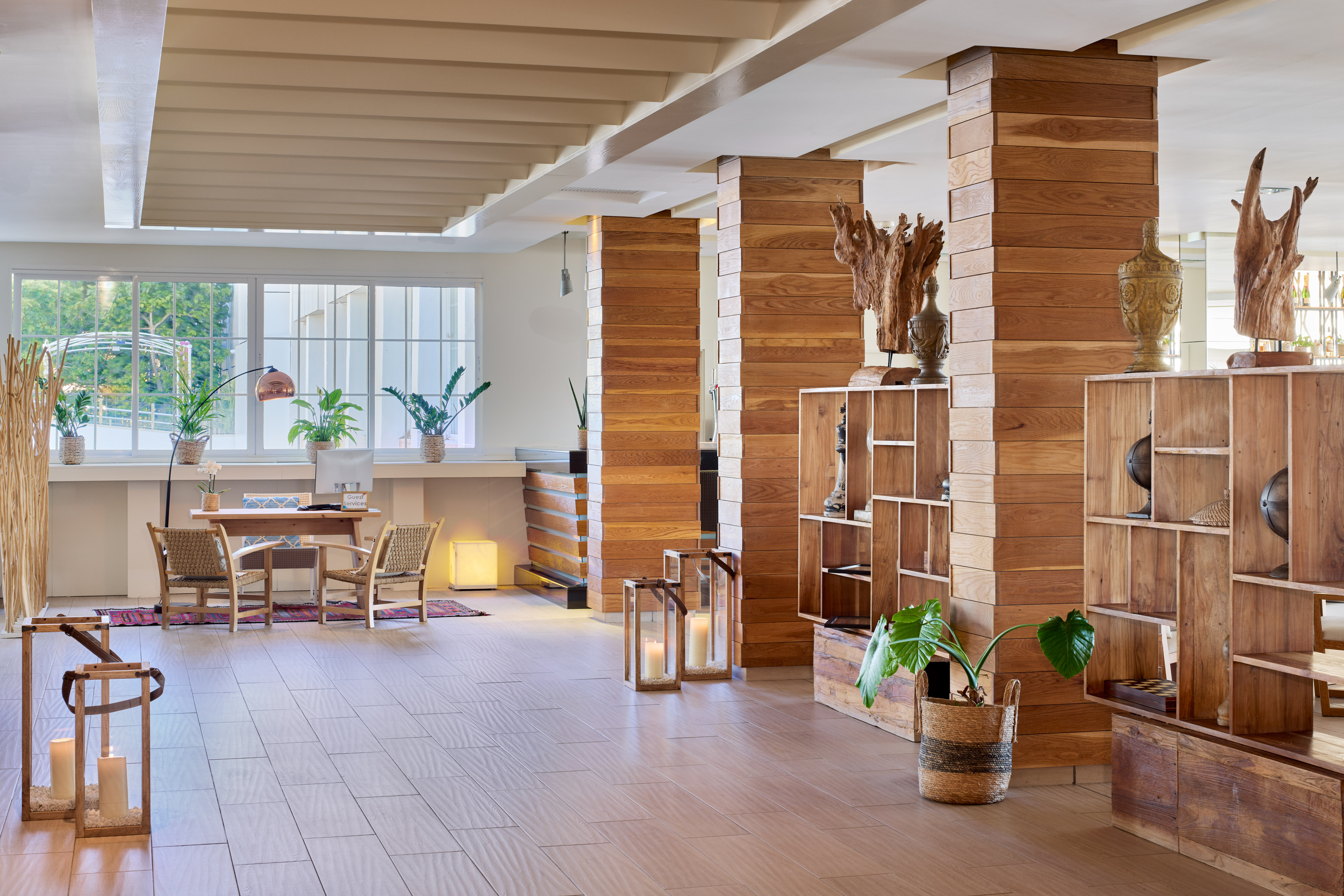 Modern resort lobby with wooden pillars, large windows, and green plants.