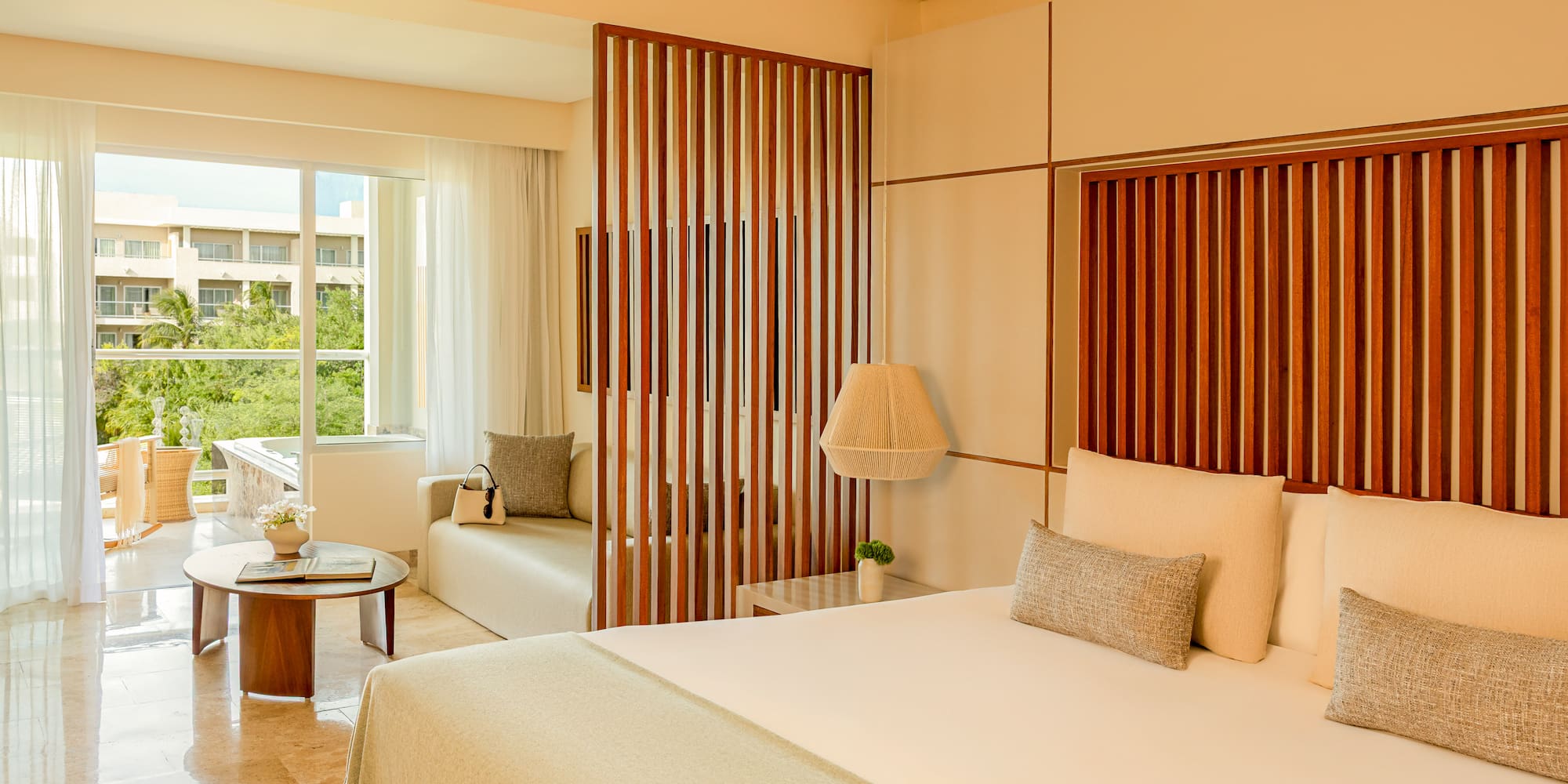 Modern tropical hotel suite with king bed, wooden divider, and balcony.