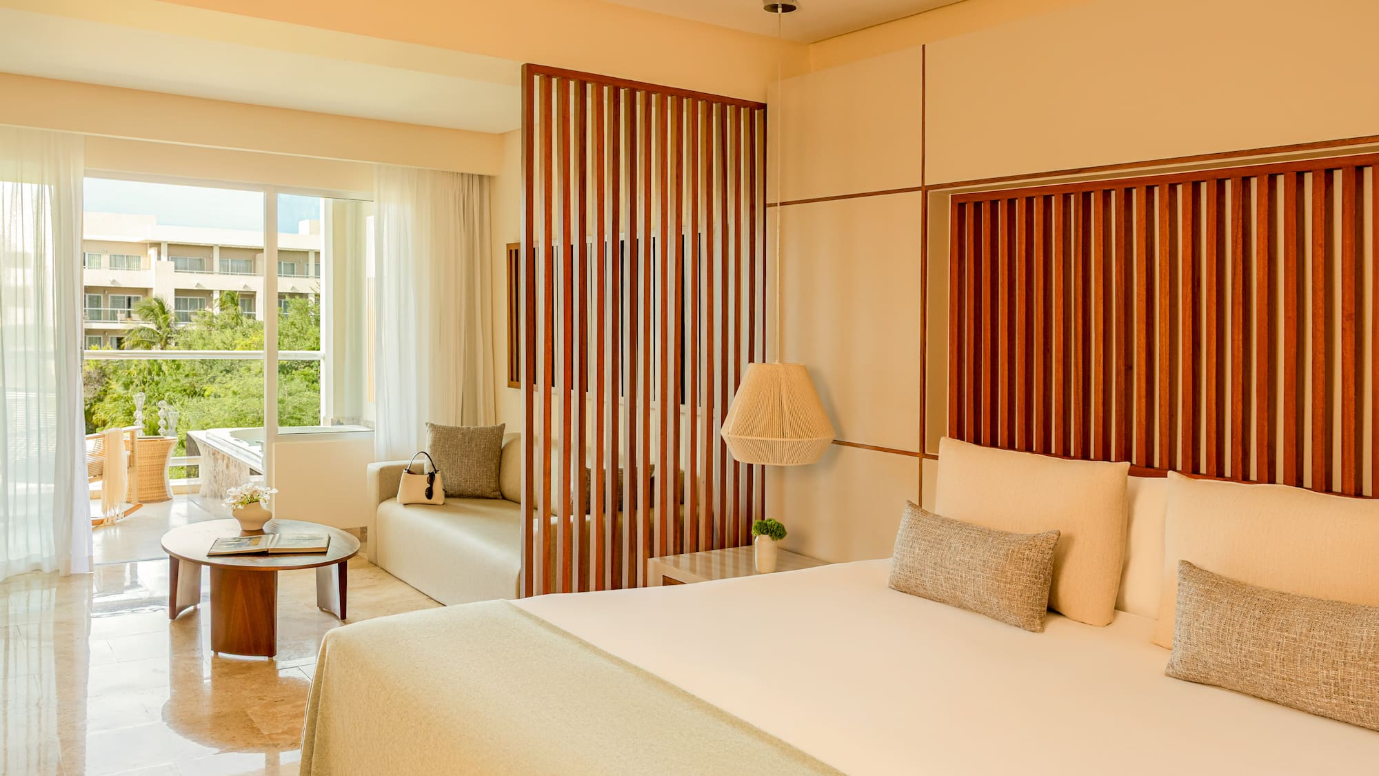 Modern tropical hotel suite with king bed, wooden divider, and balcony.