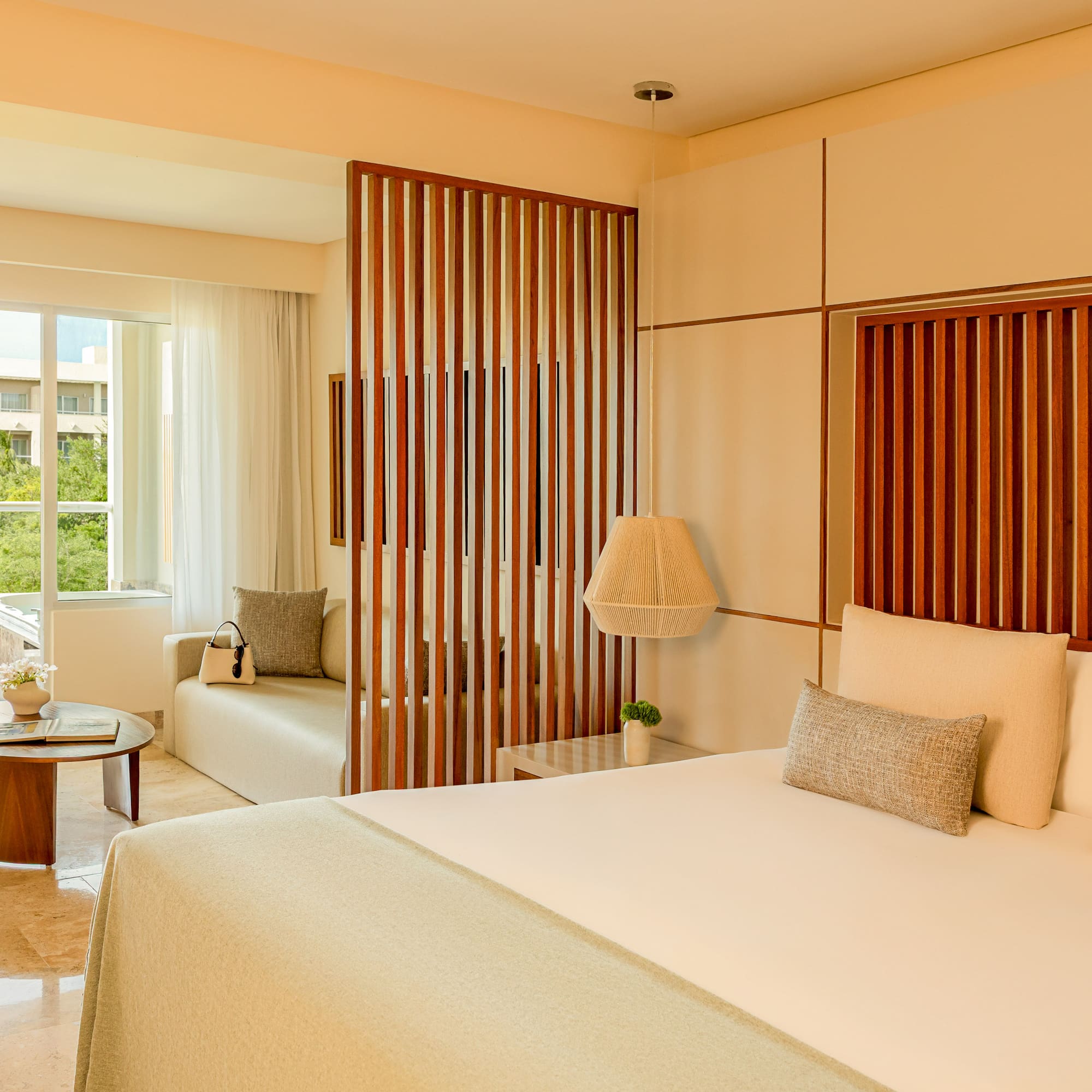 Modern tropical hotel suite with king bed, wooden divider, and balcony.