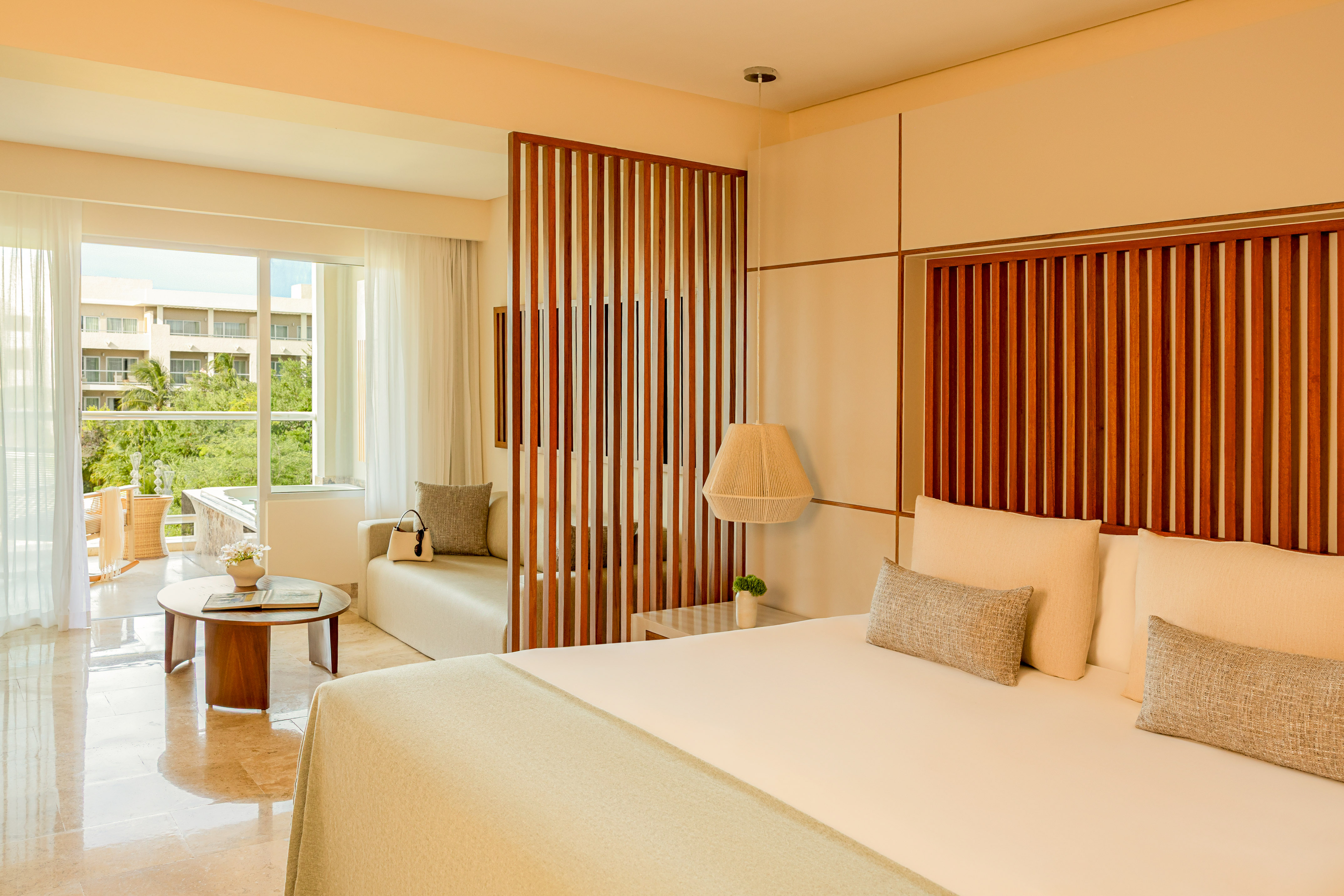 Modern tropical hotel suite with king bed, wooden divider, and balcony.