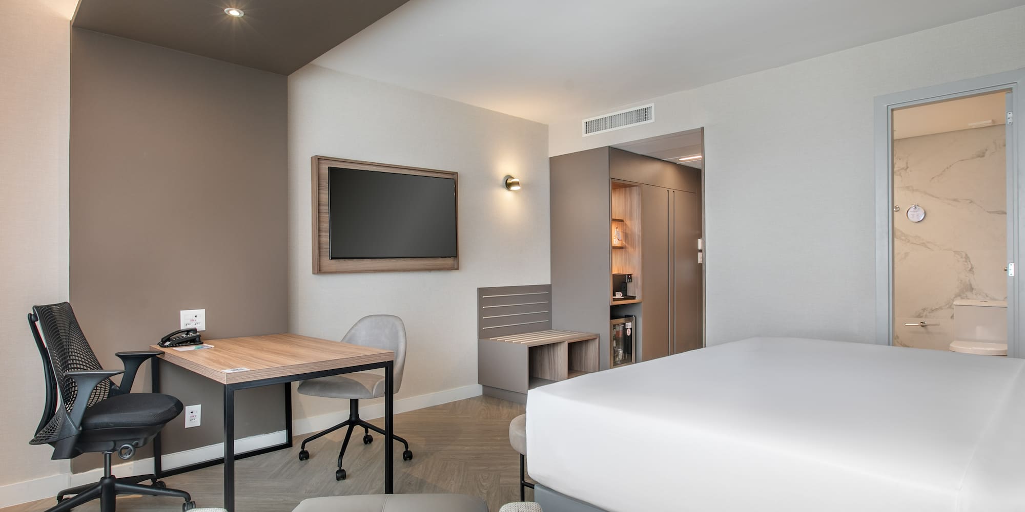 Modern hotel room with bed, work desk, TV, and marble bathroom.