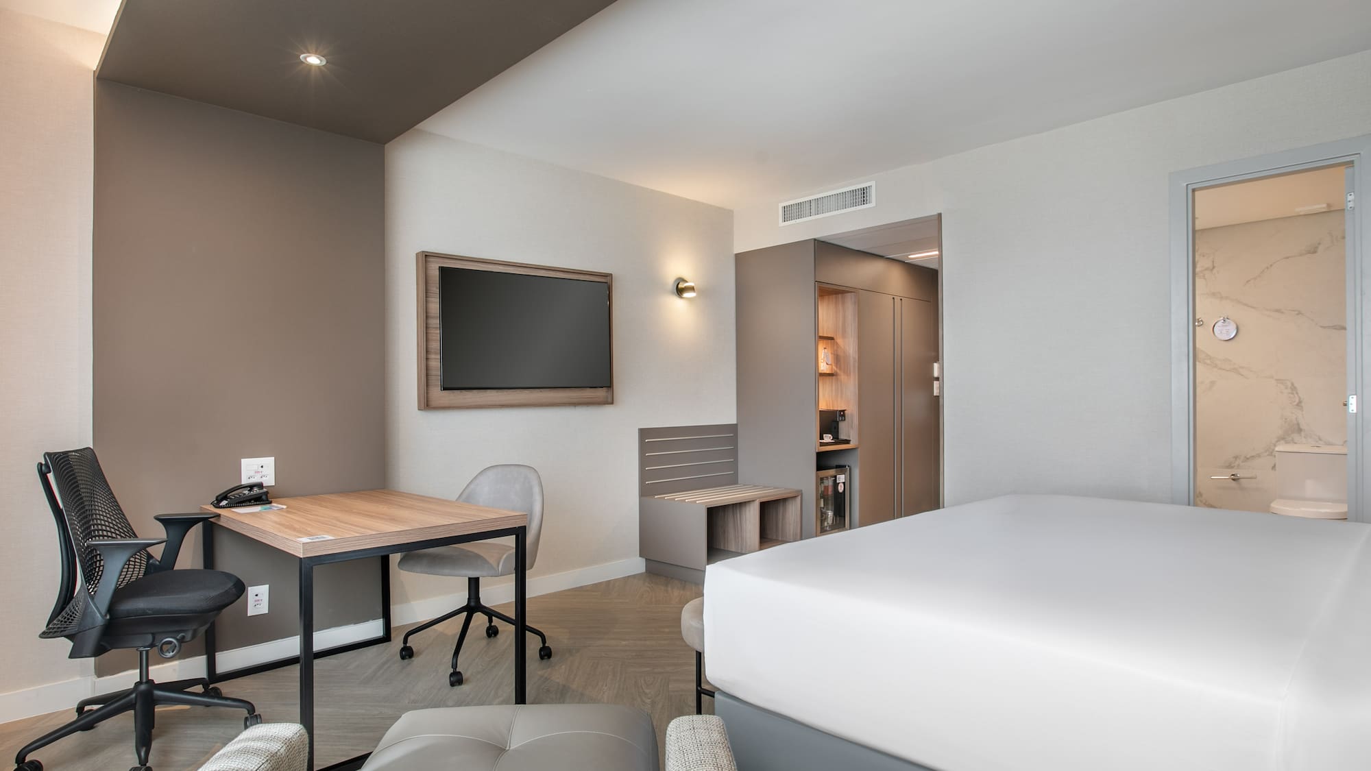 Modern hotel room with bed, work desk, TV, and marble bathroom.