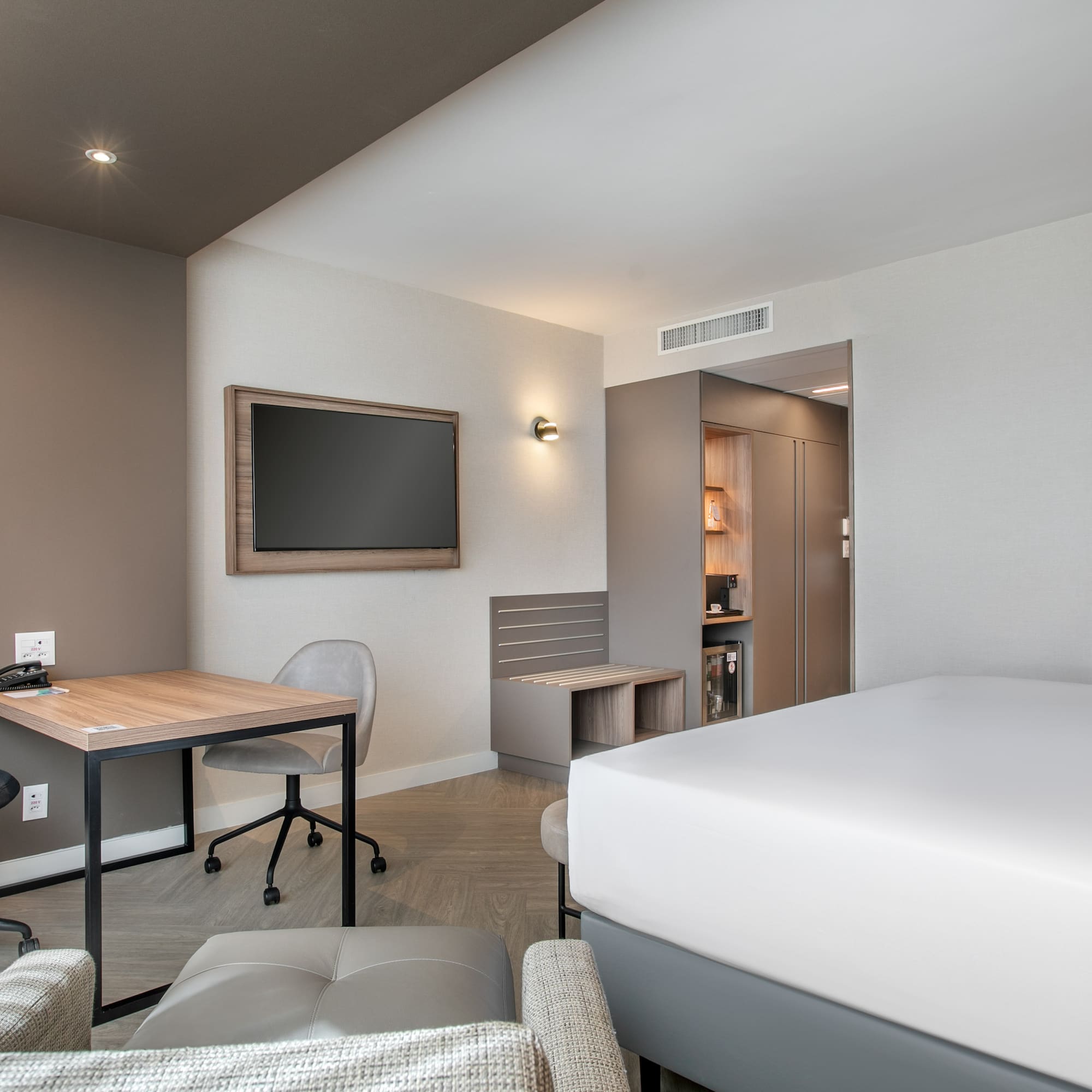 Contemporary hotel room with bed, work desk, wall TV, and mini-bar.