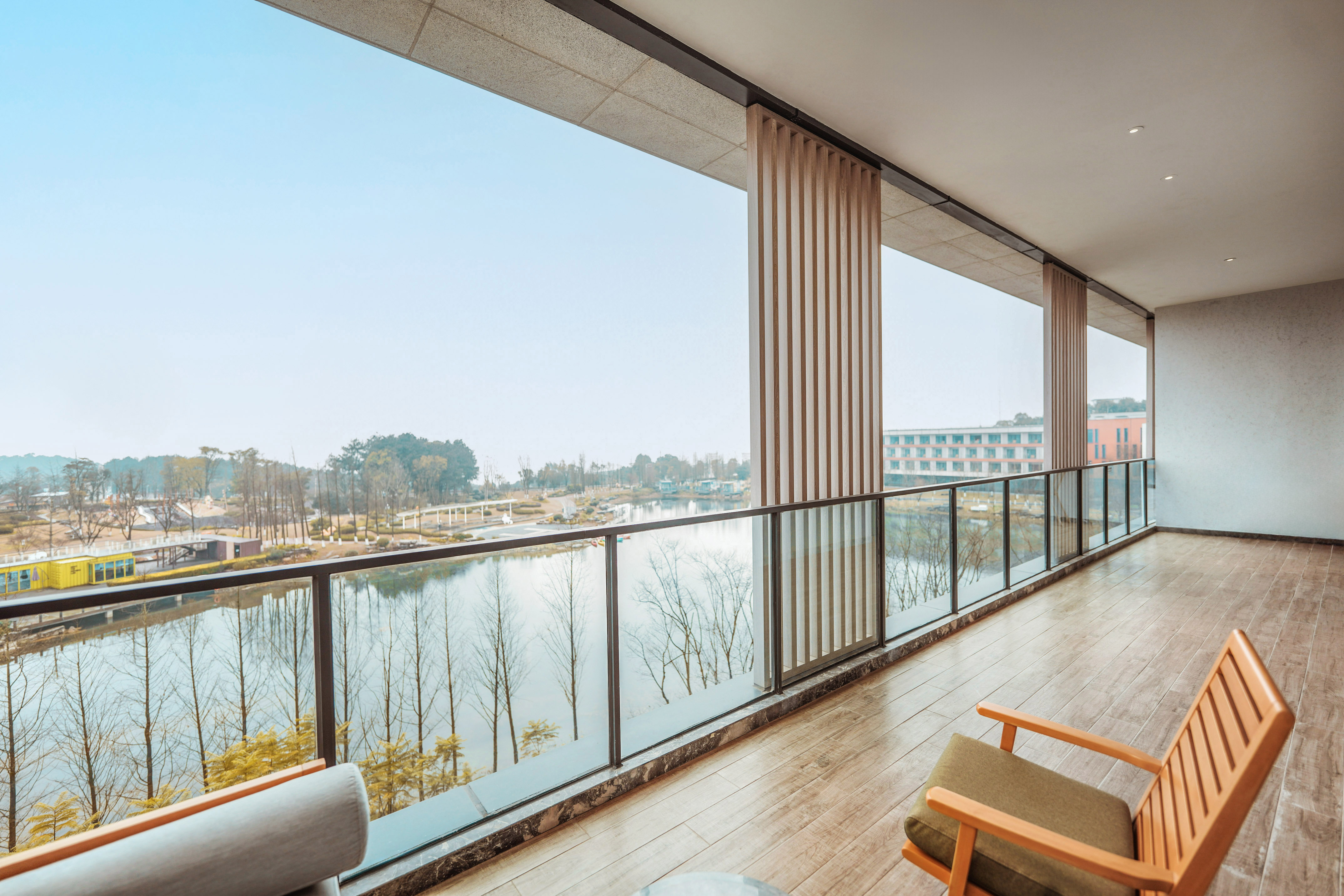 Modern balcony with lake view, glass railing, wood floor, and lounge chairs.