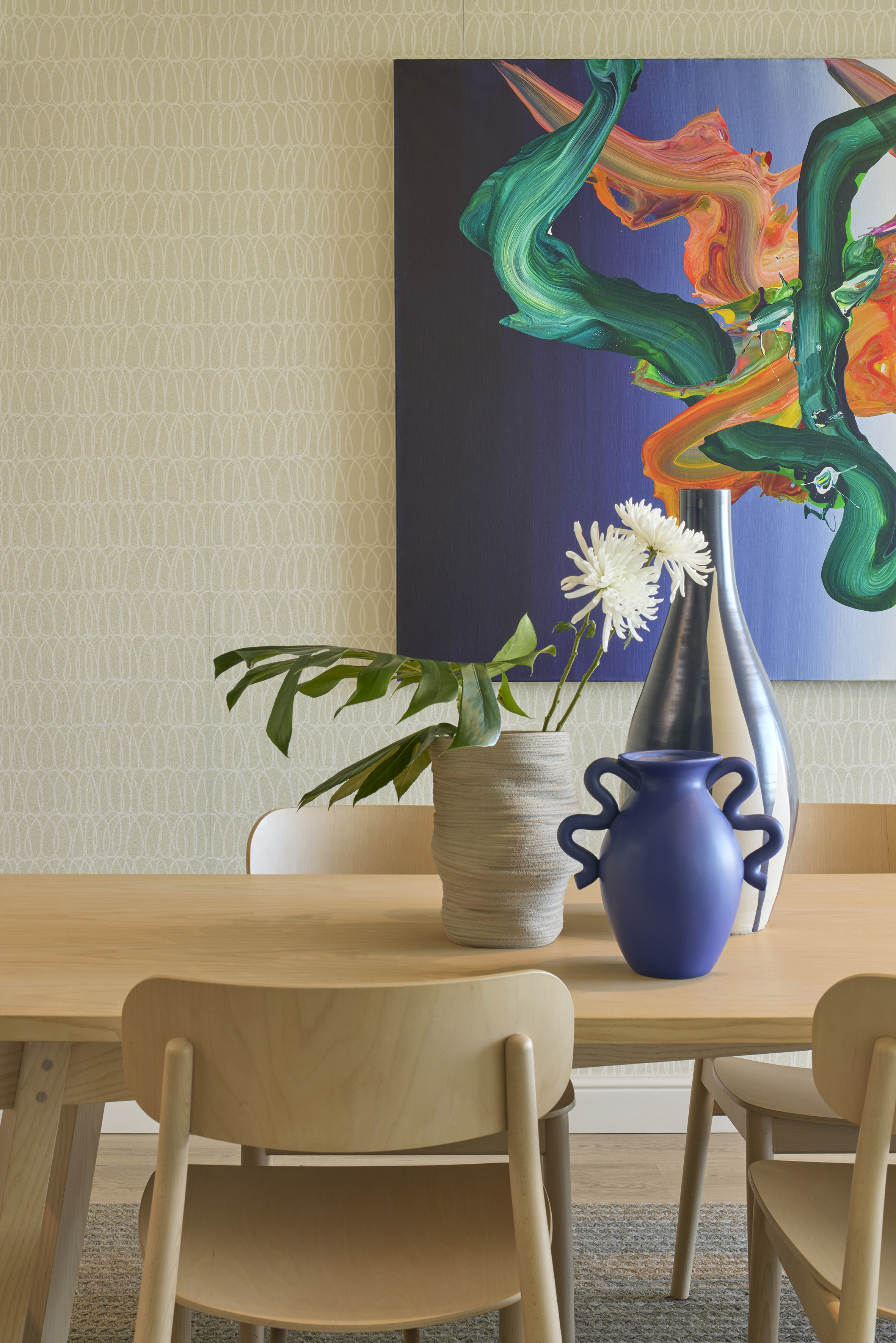 Modern dining room with abstract art, light wood table, and decorative vases.
