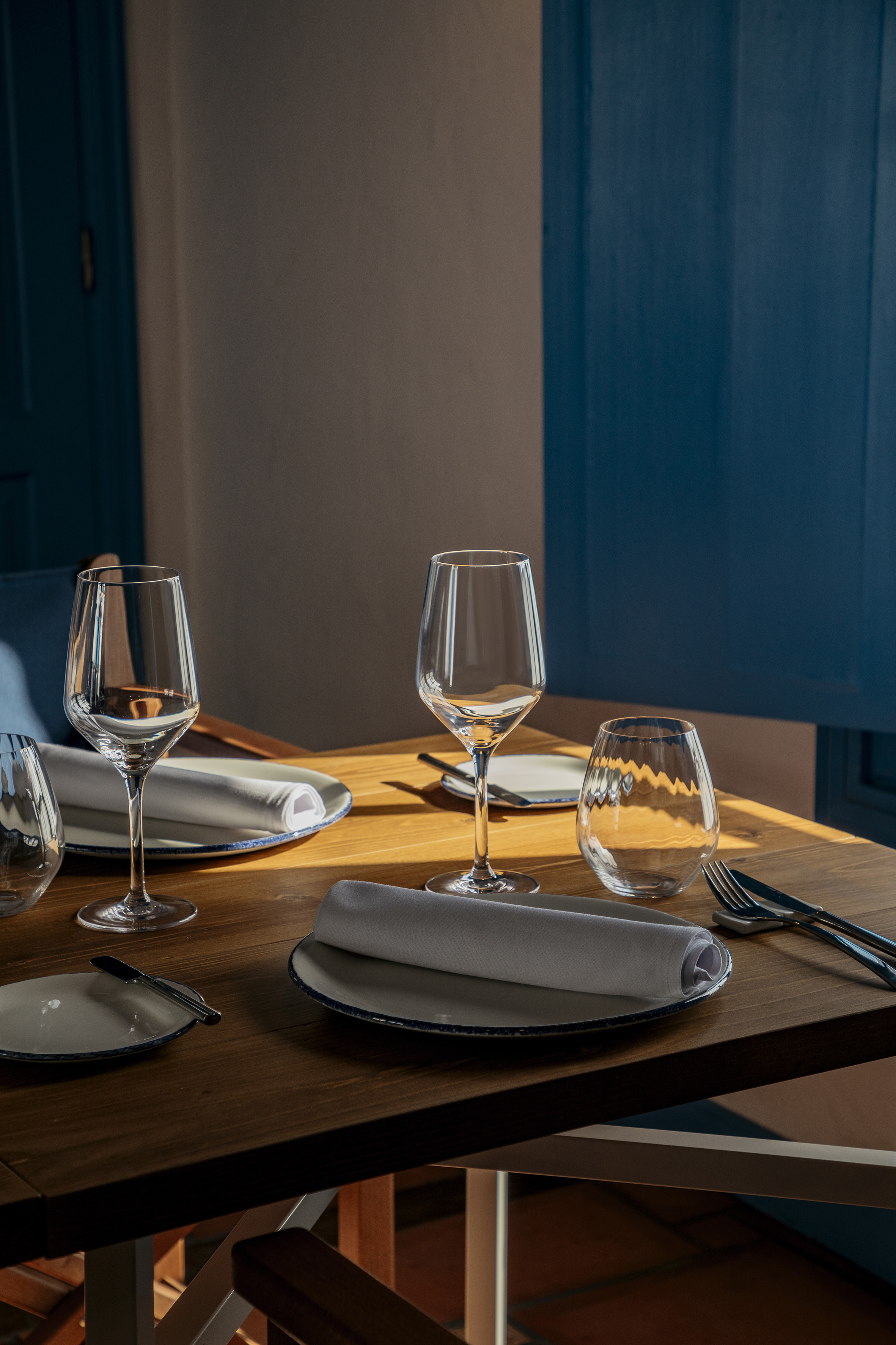 Restaurant table set with plates, rolled napkins, wine glasses, and cutlery.