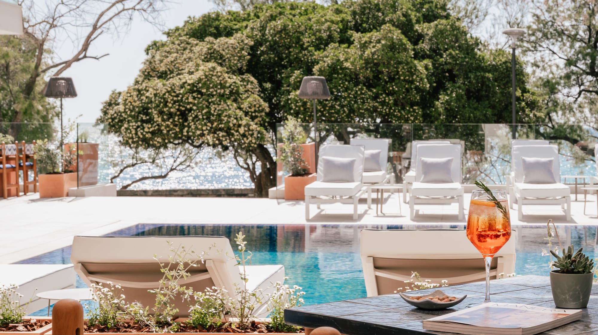 Orange cocktail on table by resort pool, sun loungers, and sparkling ocean.