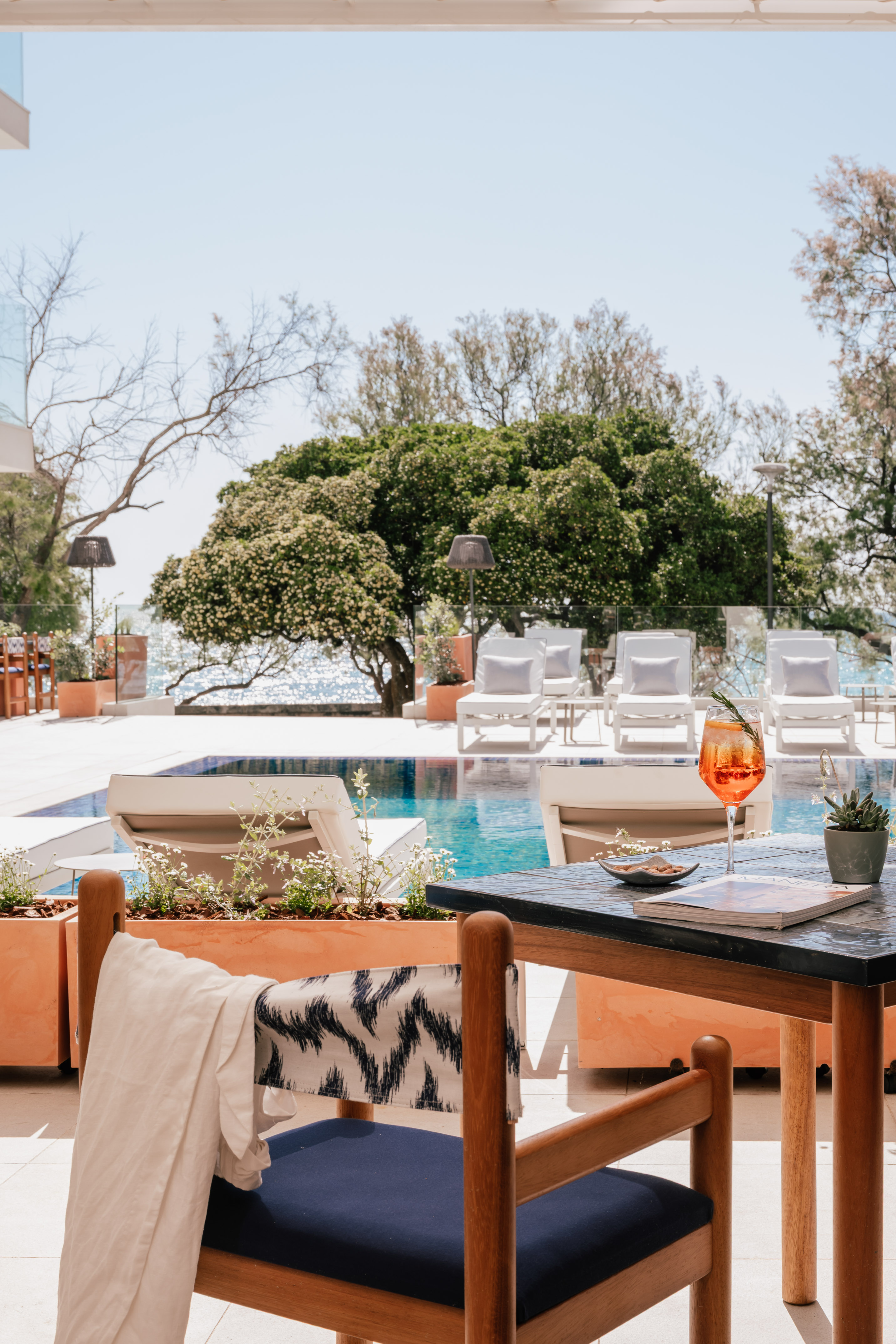 Orange cocktail on table by resort pool, sun loungers, and sparkling ocean.