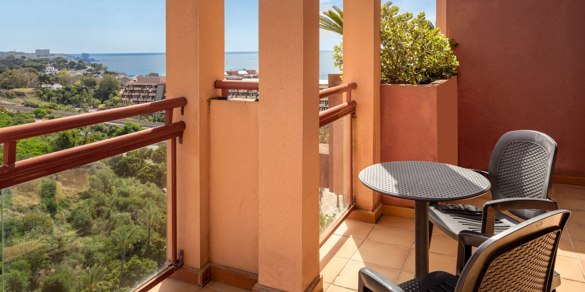 Terracotta balcony with outdoor seating, scenic sea view, and coastal resort.