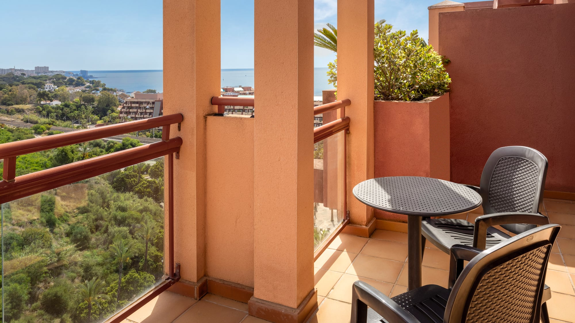 Terracotta balcony with outdoor seating, scenic sea view, and coastal resort.