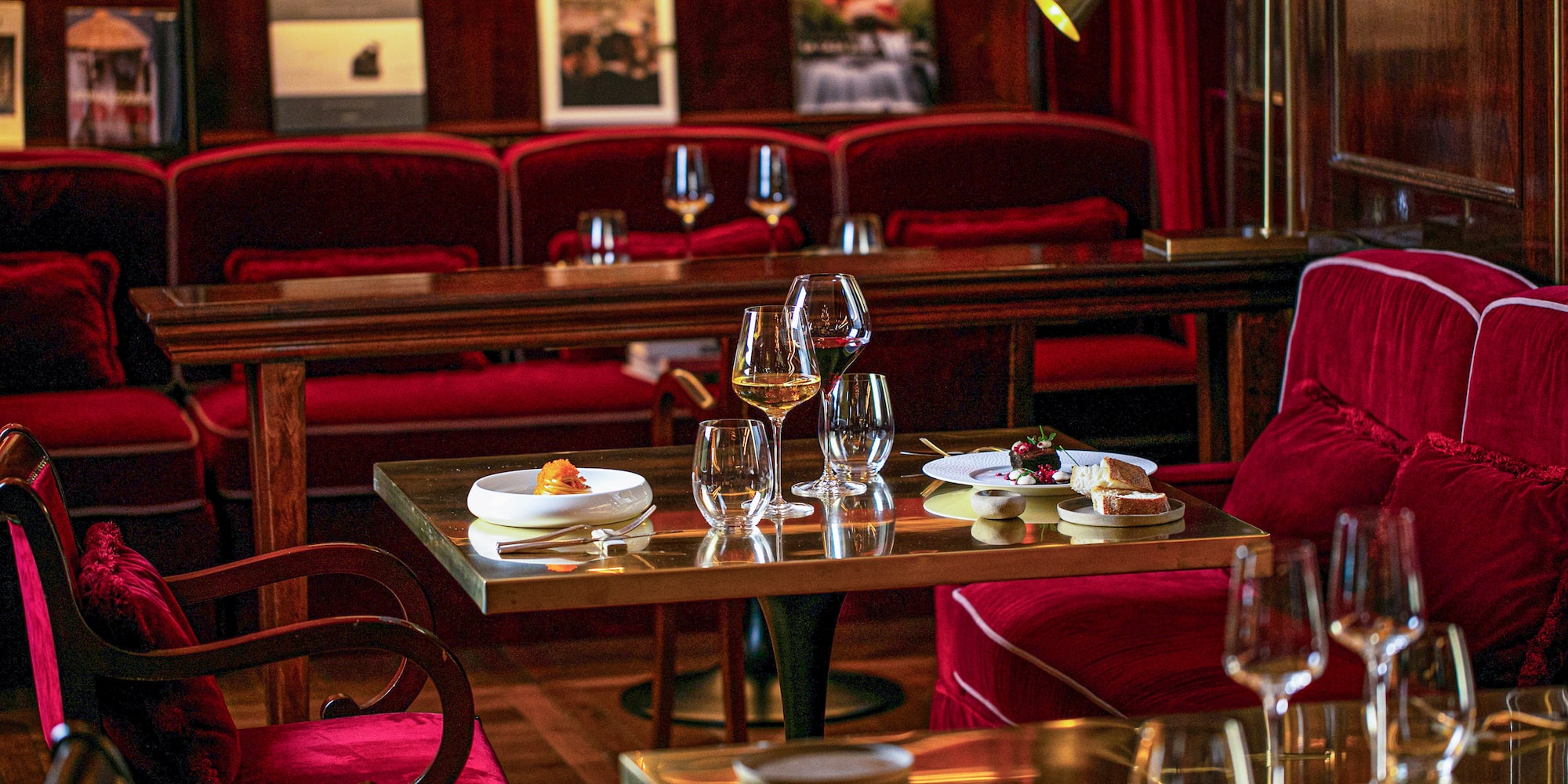 Elegant fine dining room with red velvet seats, wine, and small plates.