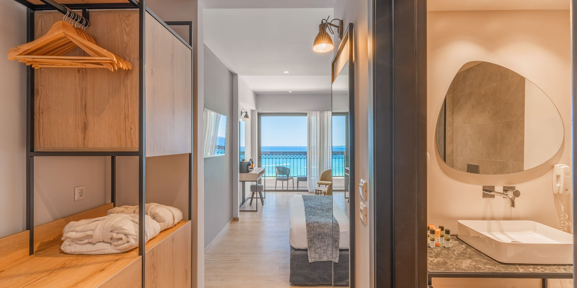 Modern hotel room with sea view balcony, open closet, and bathroom vanity.