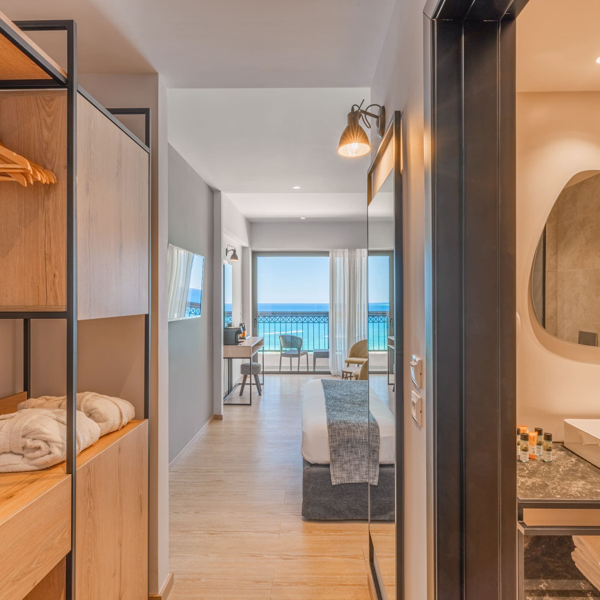 Modern hotel room with sea view balcony, open closet, and bathroom vanity.