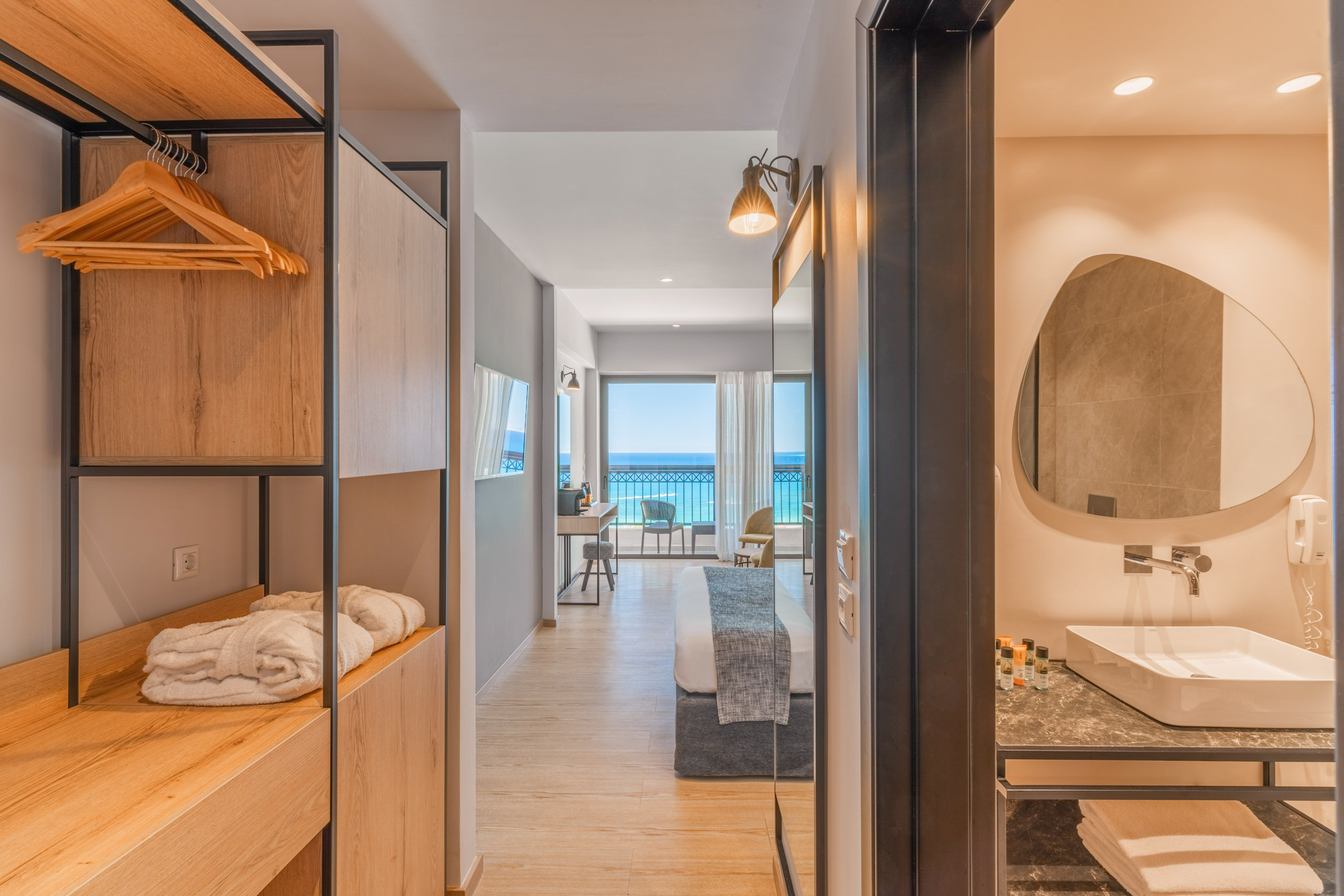 Modern hotel room with sea view balcony, open closet, and bathroom vanity.