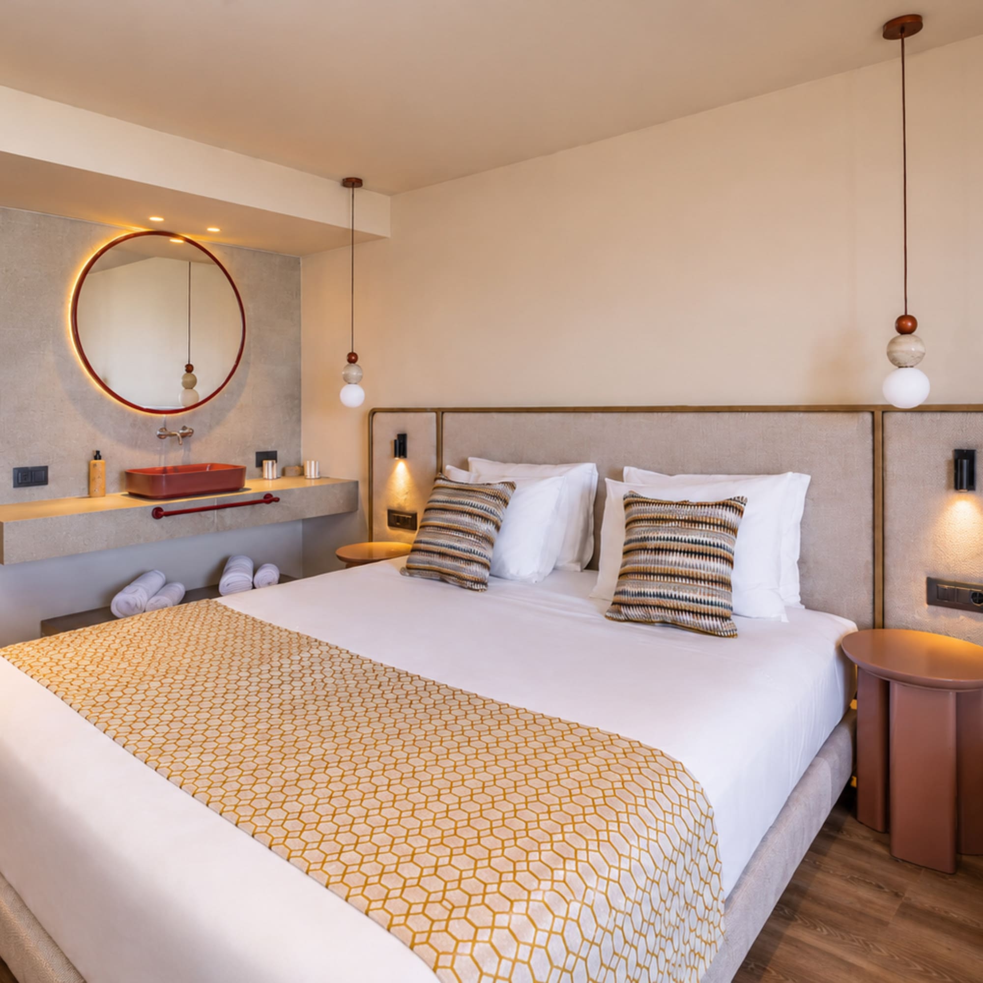 Modern hotel bedroom, bed with geometric runner, vanity, and round backlit mirror.