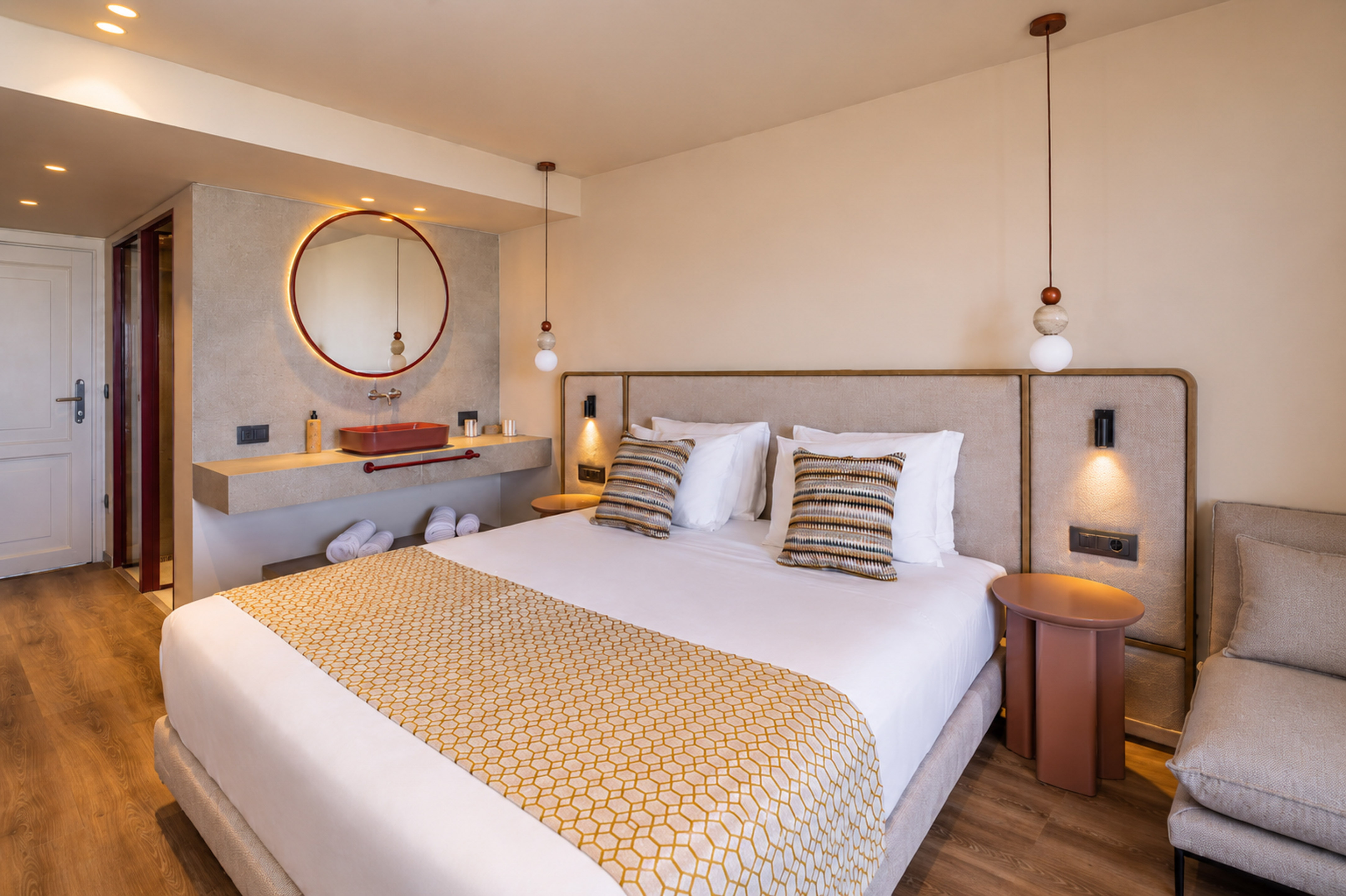Modern hotel bedroom, bed with geometric runner, vanity, and round backlit mirror.