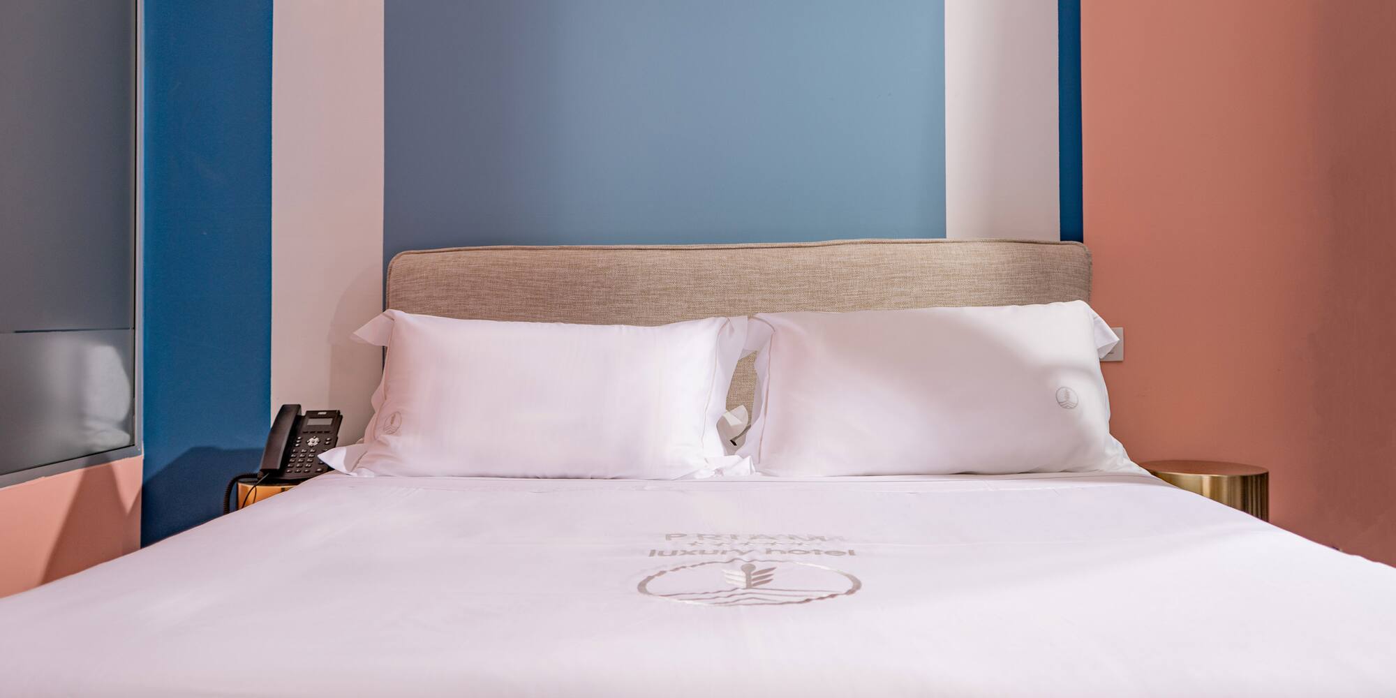 Modern luxury hotel bed with white sheets, beige headboard, colorful walls.