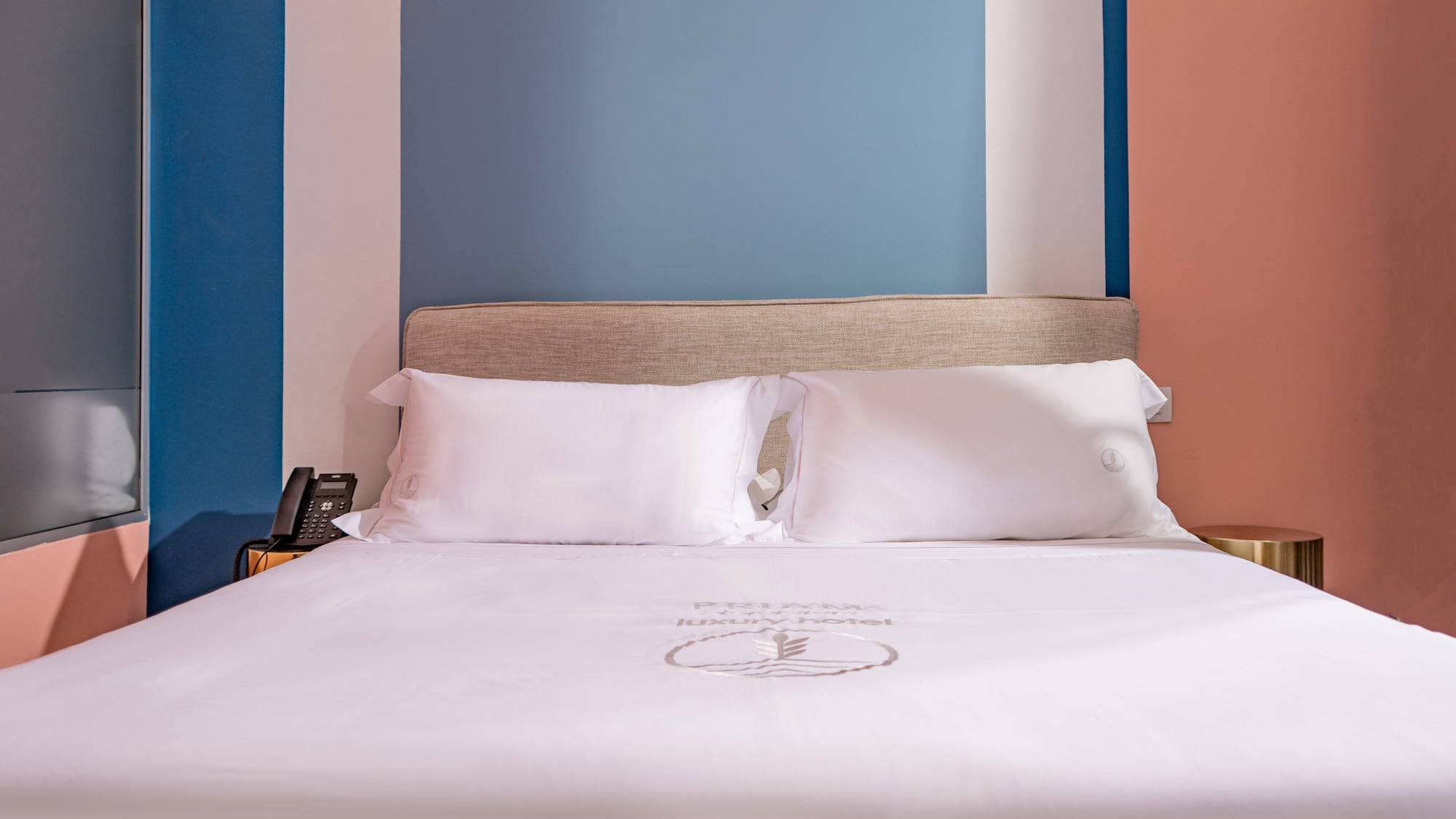 Modern luxury hotel bed with white sheets, beige headboard, colorful walls.