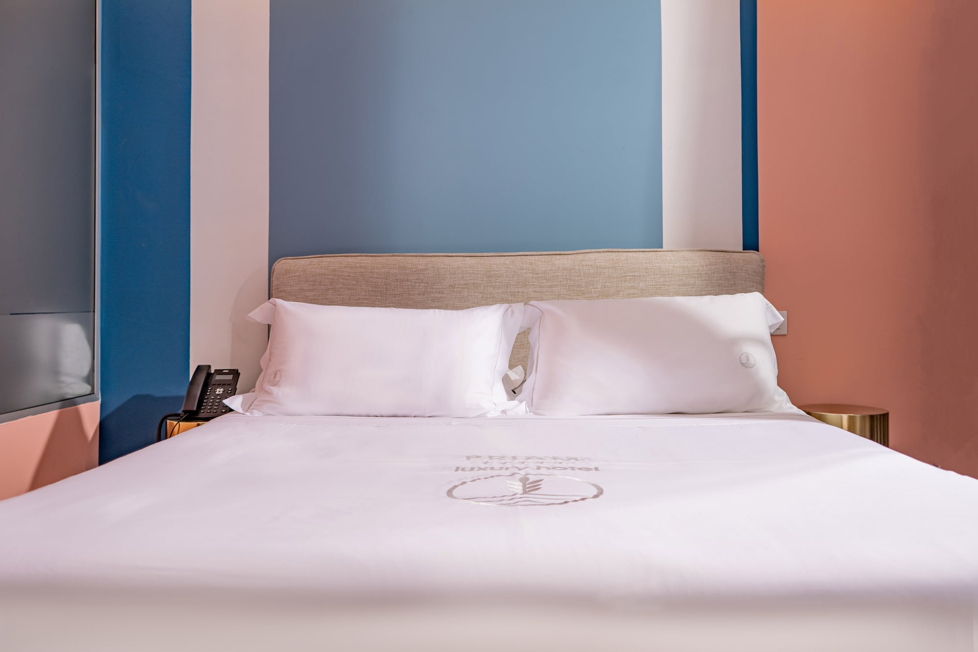 Modern luxury hotel bed with white sheets, beige headboard, colorful walls.