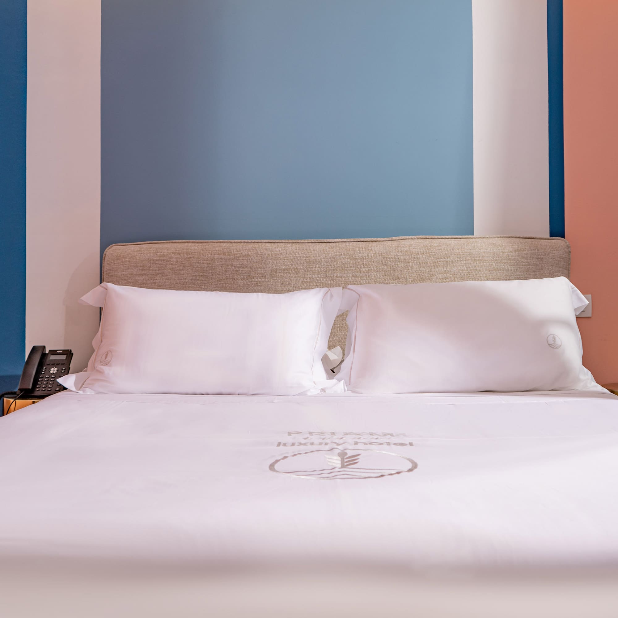 Modern luxury hotel bed with white sheets, beige headboard, colorful walls.