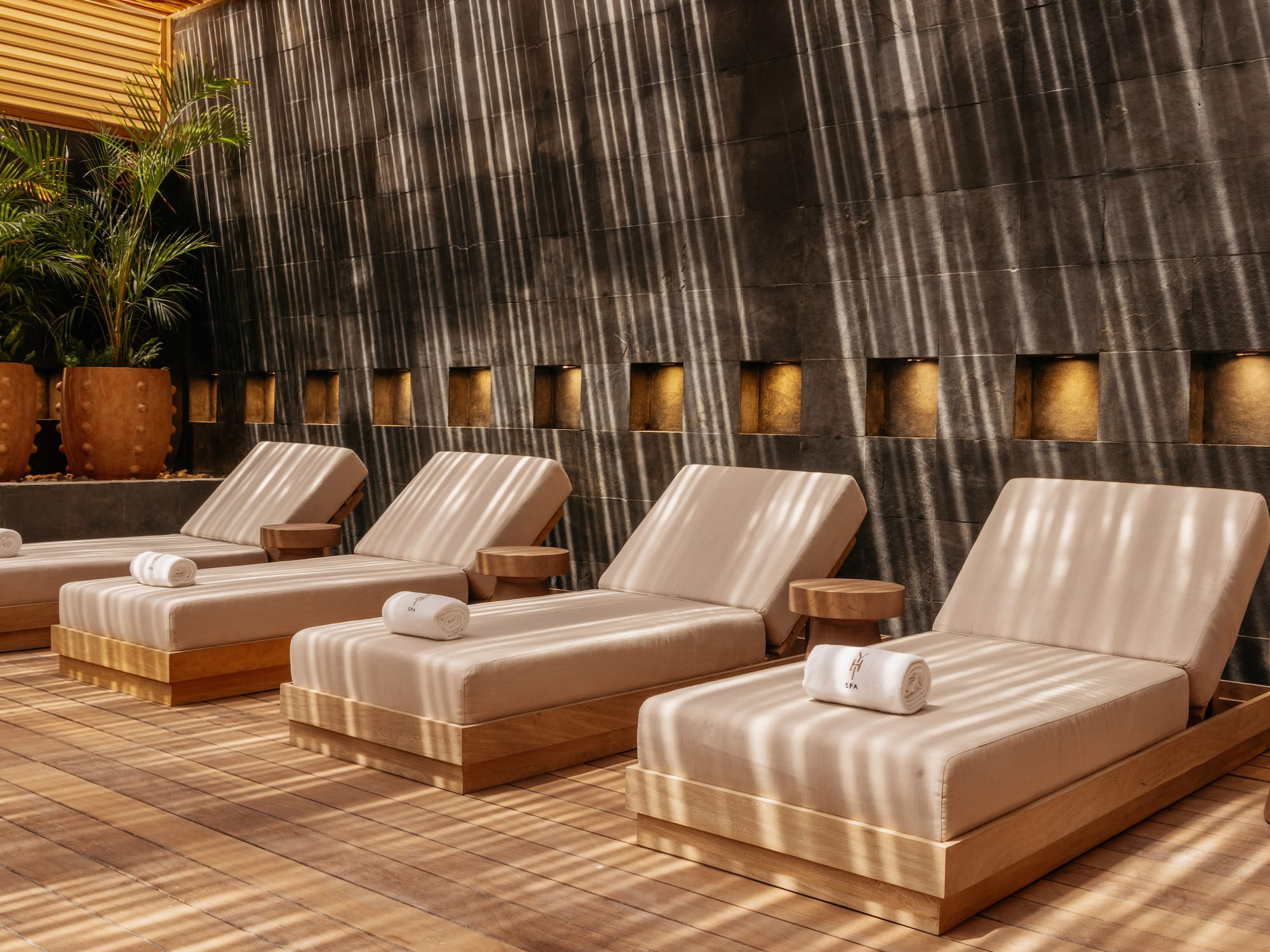 Relaxing spa lounge with beige sun loungers, wooden floor, and striped sunlight.