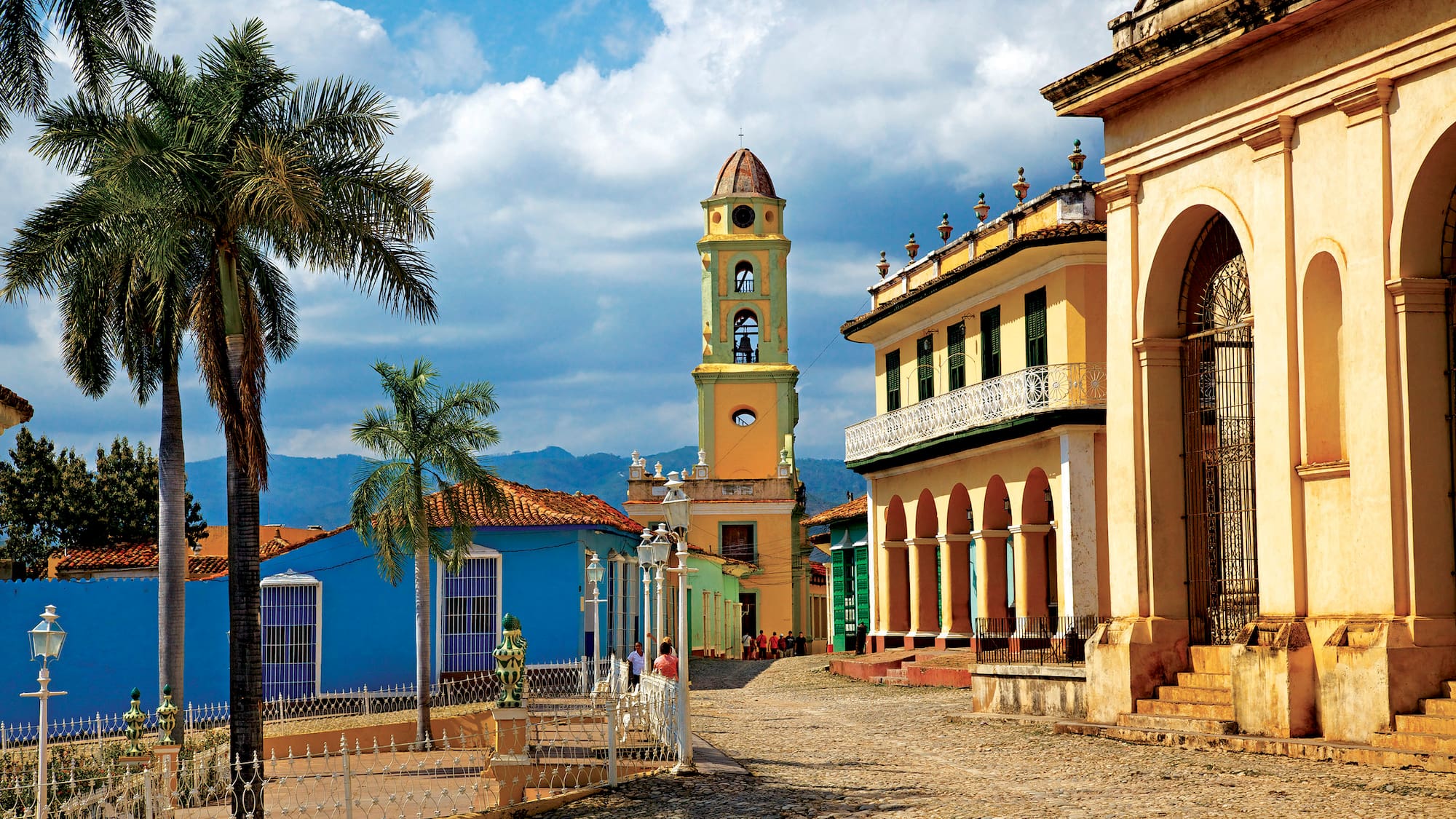 a street with a clock tower and palm trees with Trinidad in the background