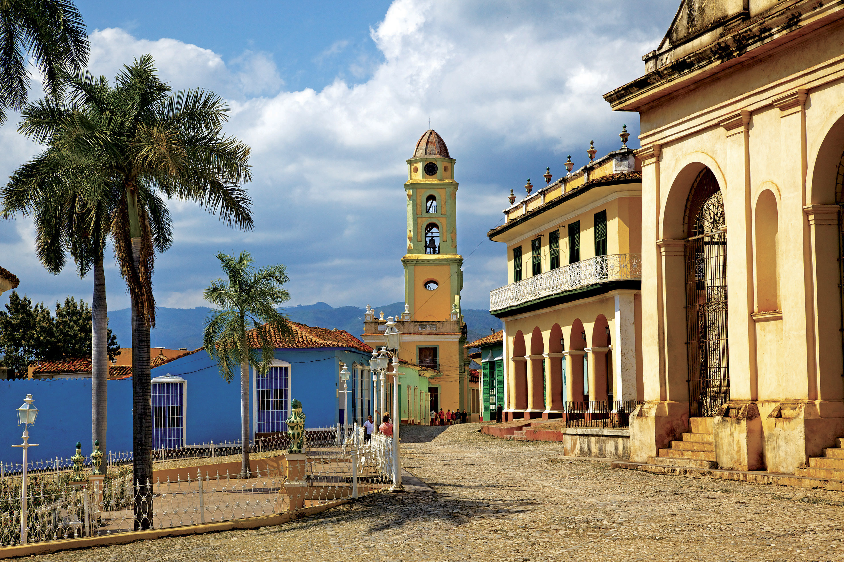 a street with a clock tower and palm trees with Trinidad in the background