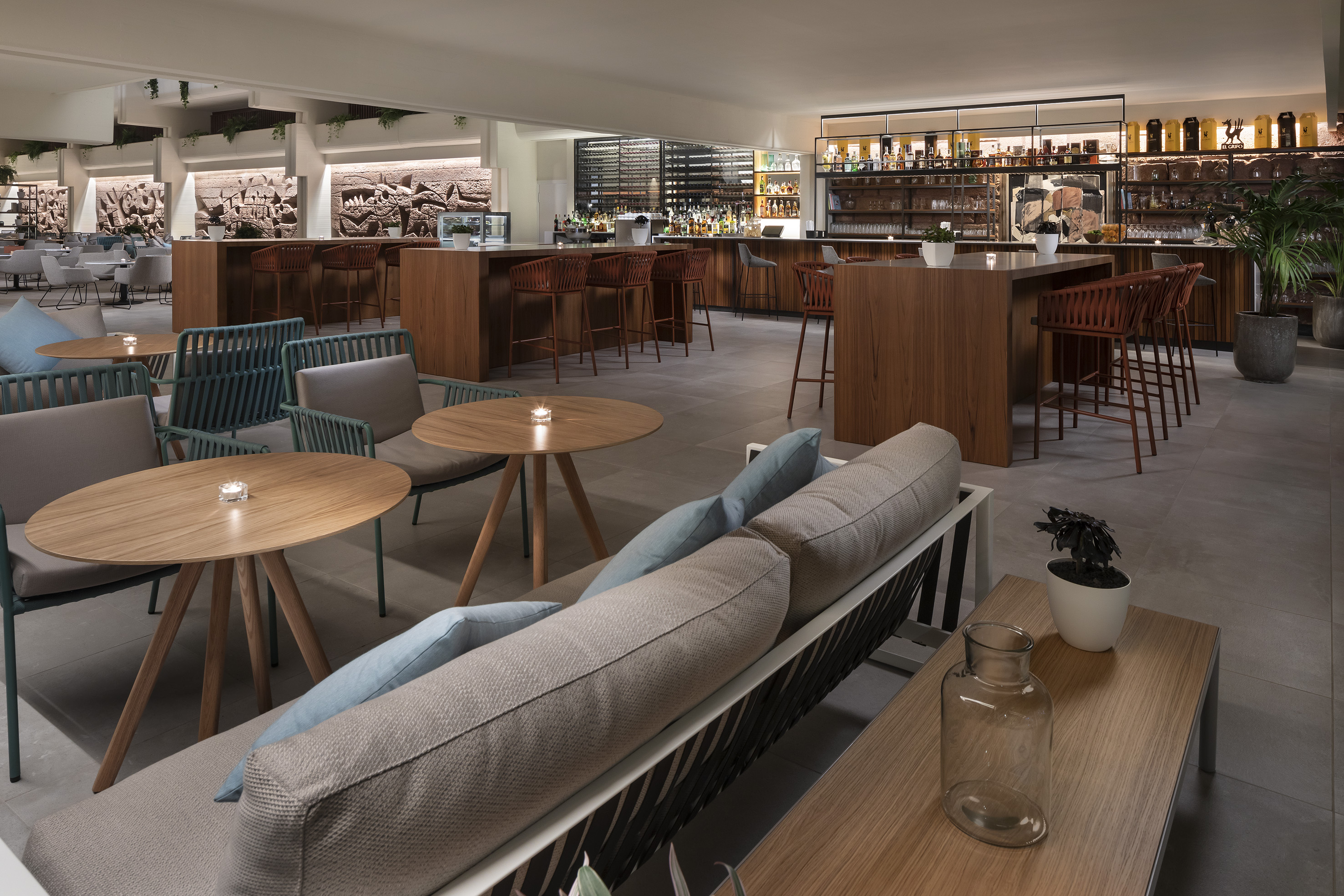 Hotel lounge bar with wooden counter, various seating, and soft ambient lighting.