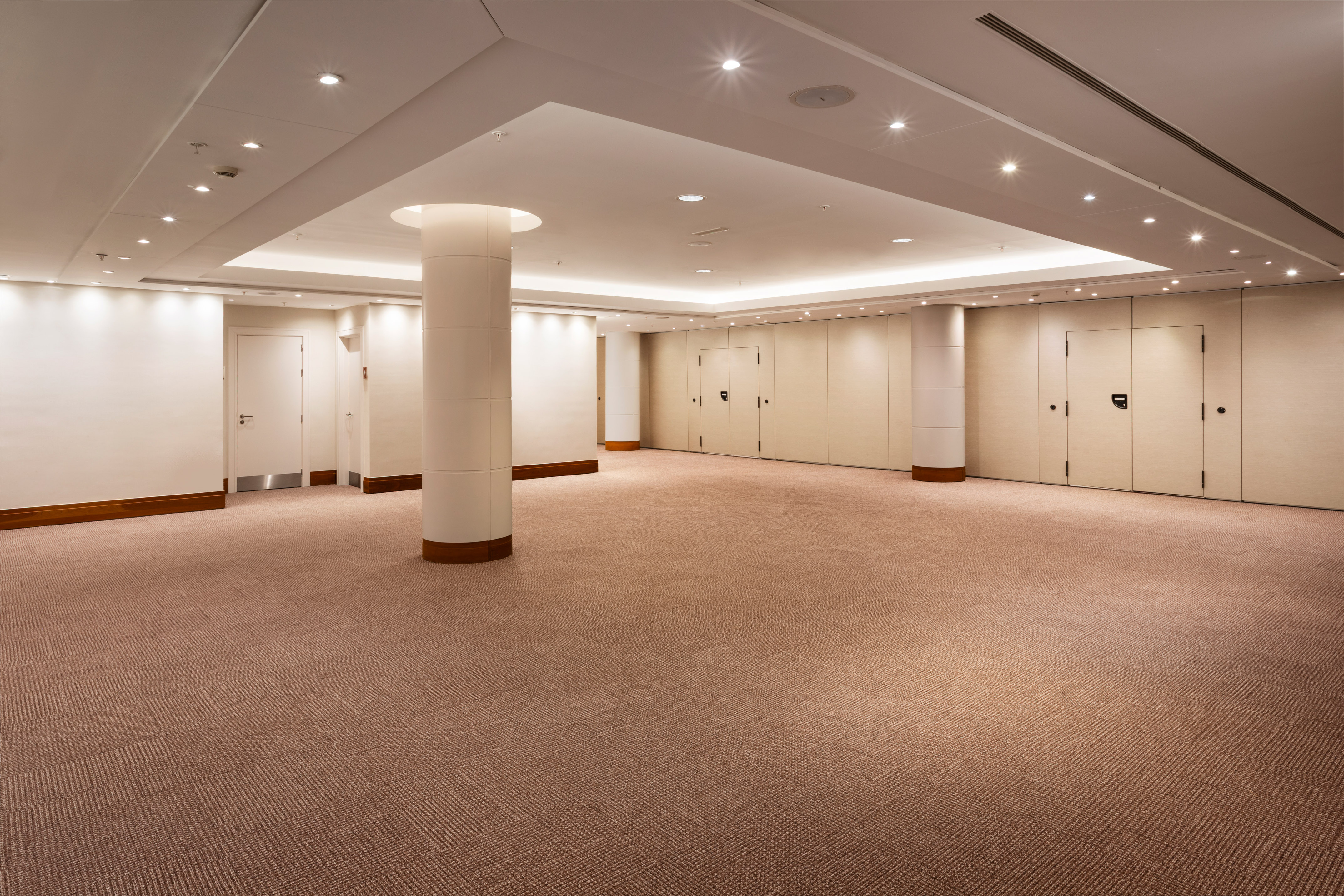 Empty modern conference room with tan carpet, white pillars, and recessed lighting.
