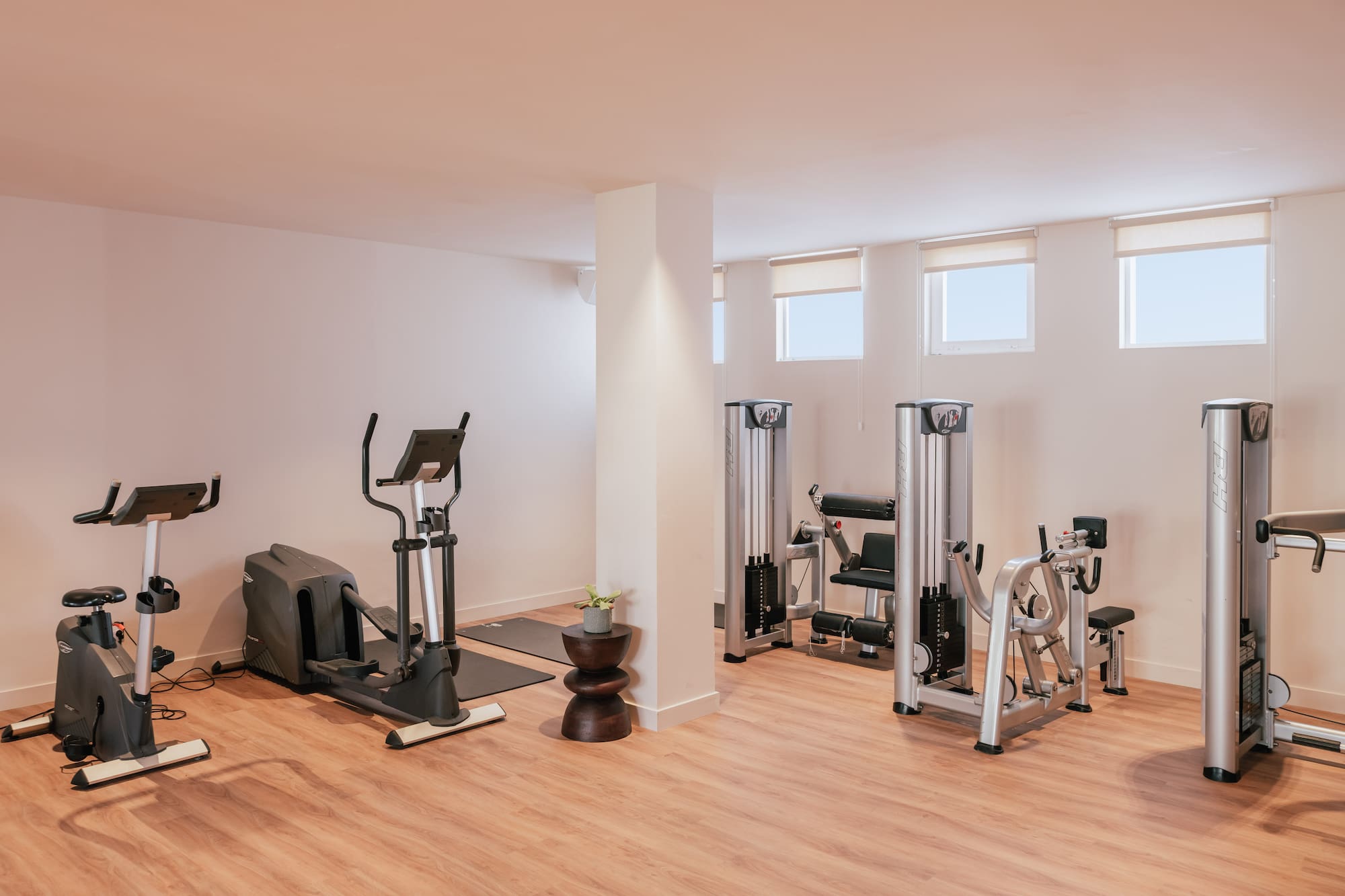 Bright modern gym with cardio and weight machines on wooden floor.