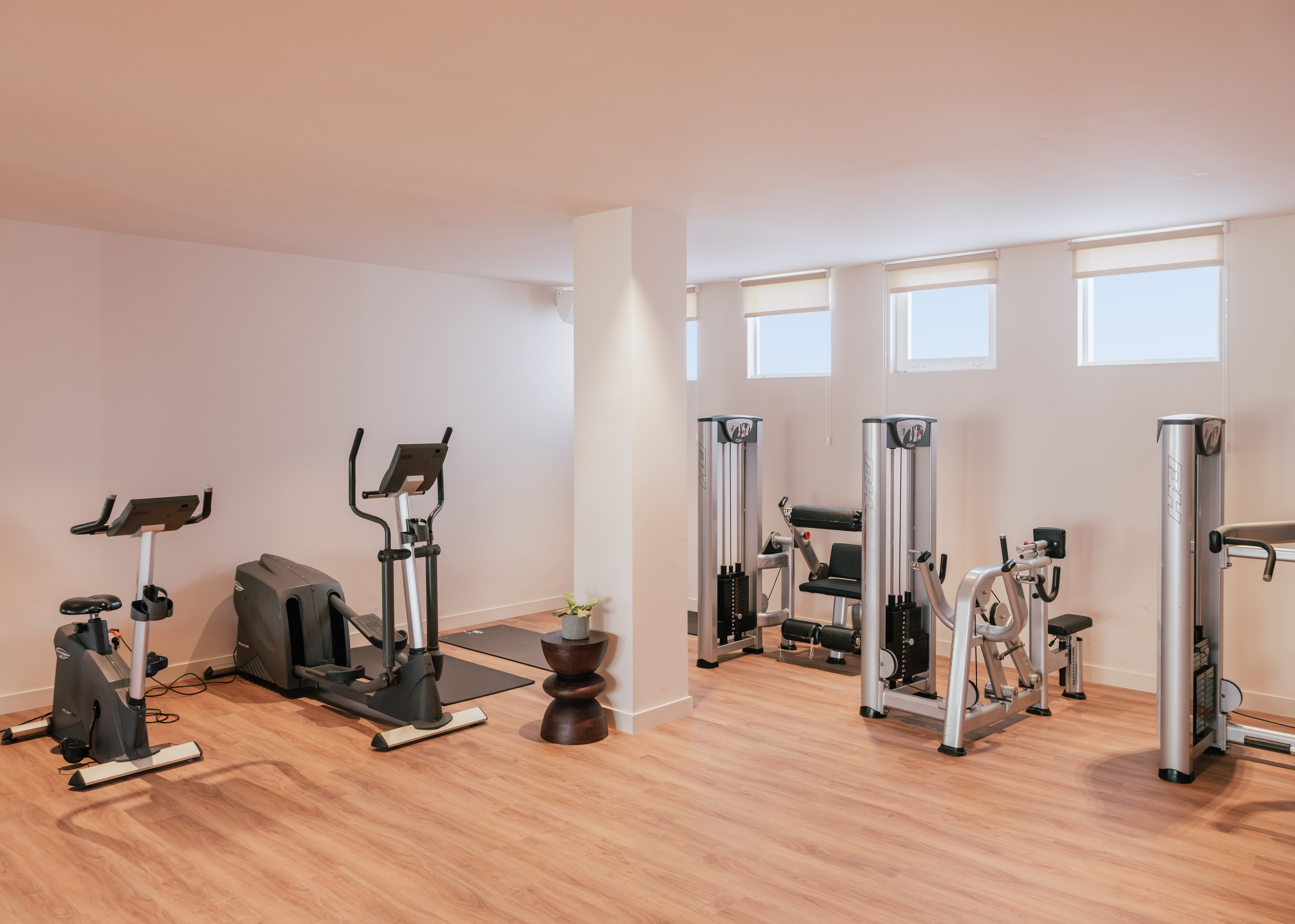 Bright modern gym with cardio and weight machines on wooden floor.
