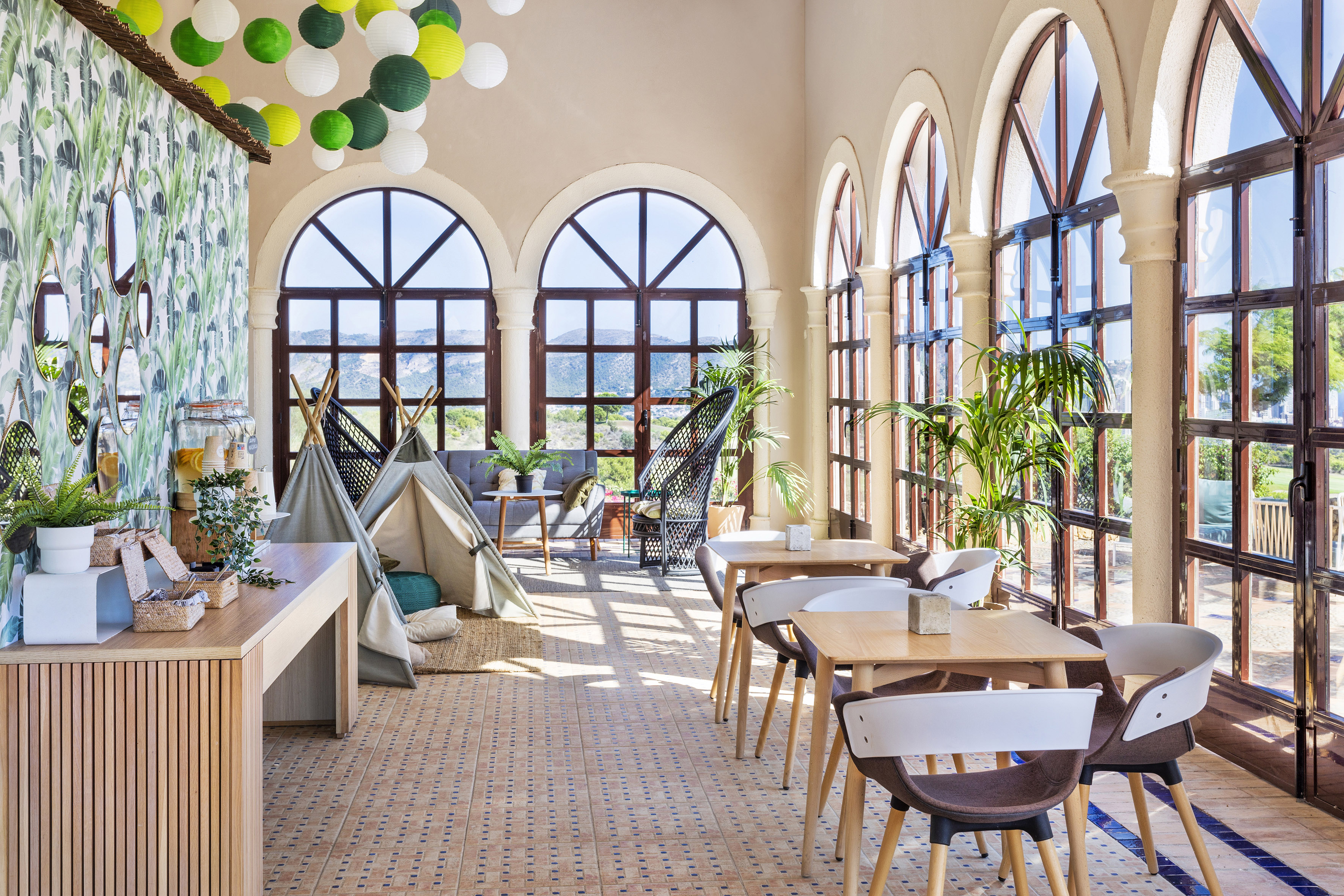 Bright lounge with arched windows, tropical decor, dining area, and kids' teepees.