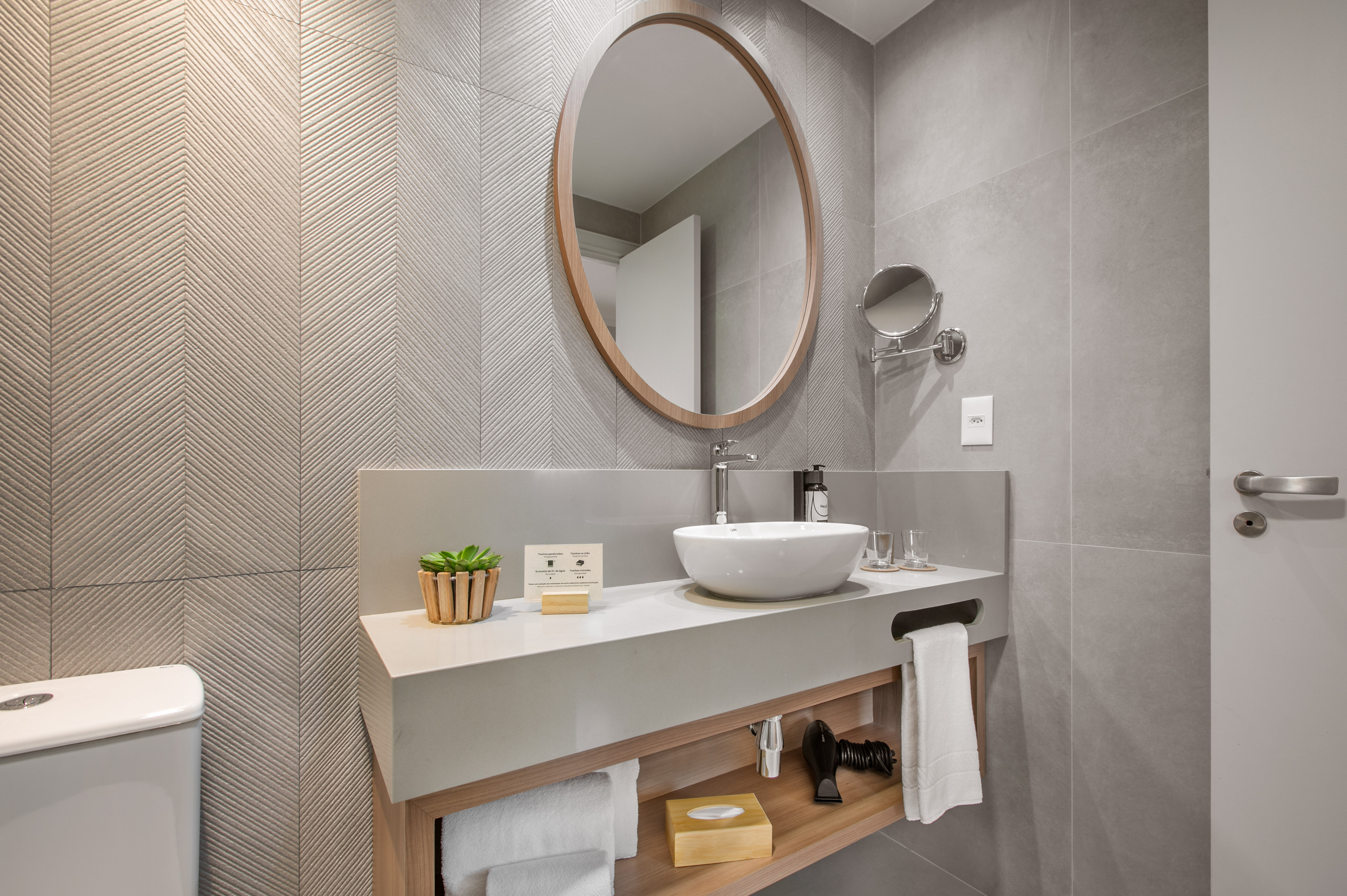 Modern bathroom vanity, round wood mirror, vessel sink, grey chevron tiles.