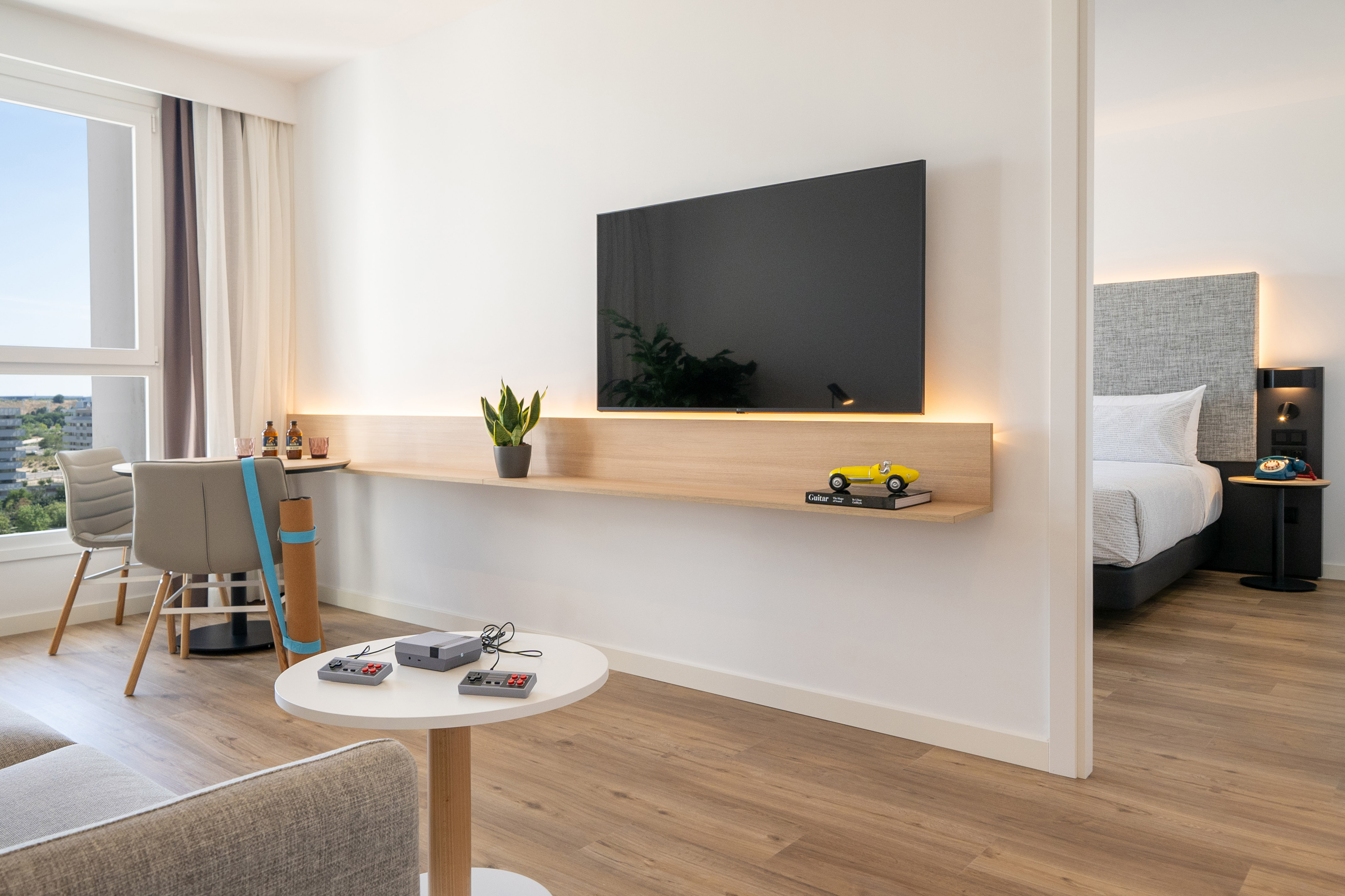 Modern hotel suite living room with TV, retro console, and bedroom access.
