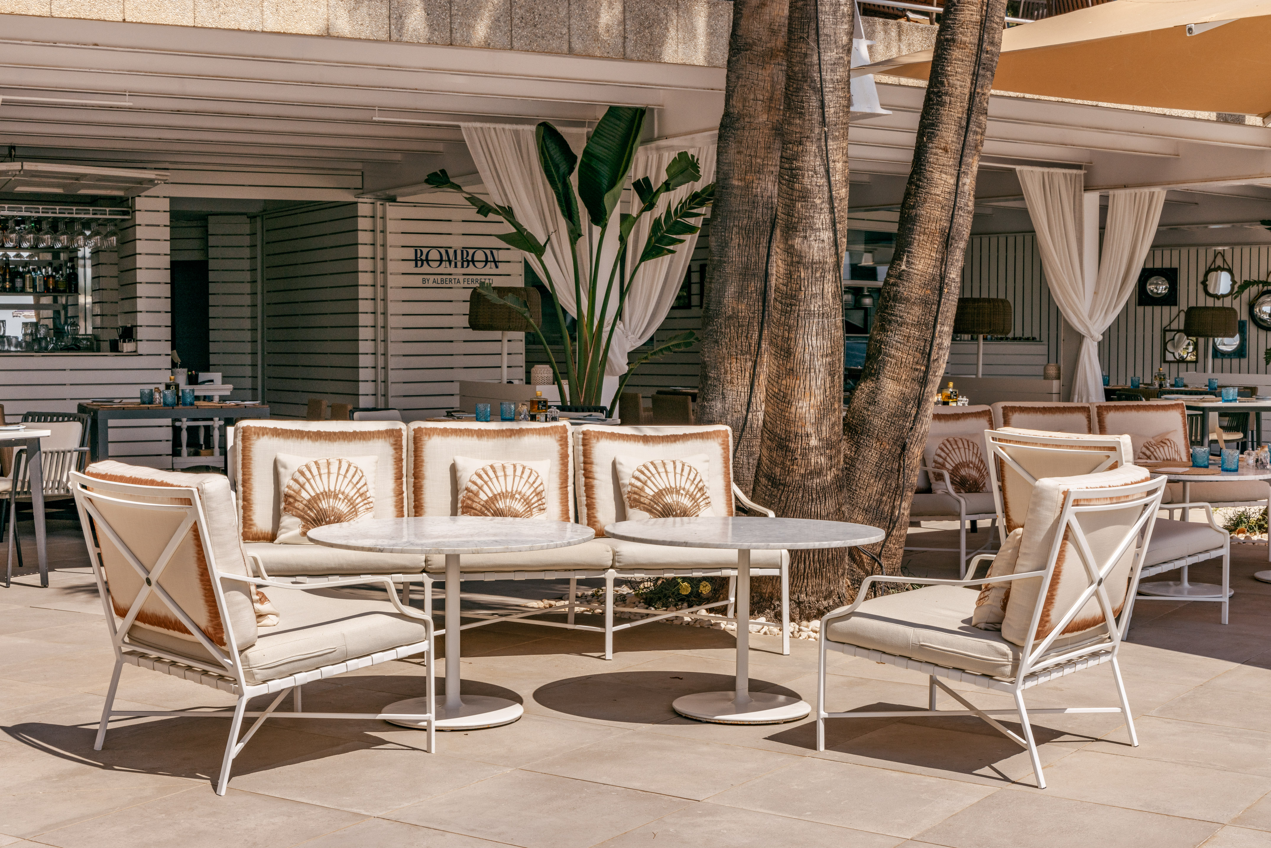 Bombon outdoor patio: white lounge furniture, seashell cushions, palm trees.