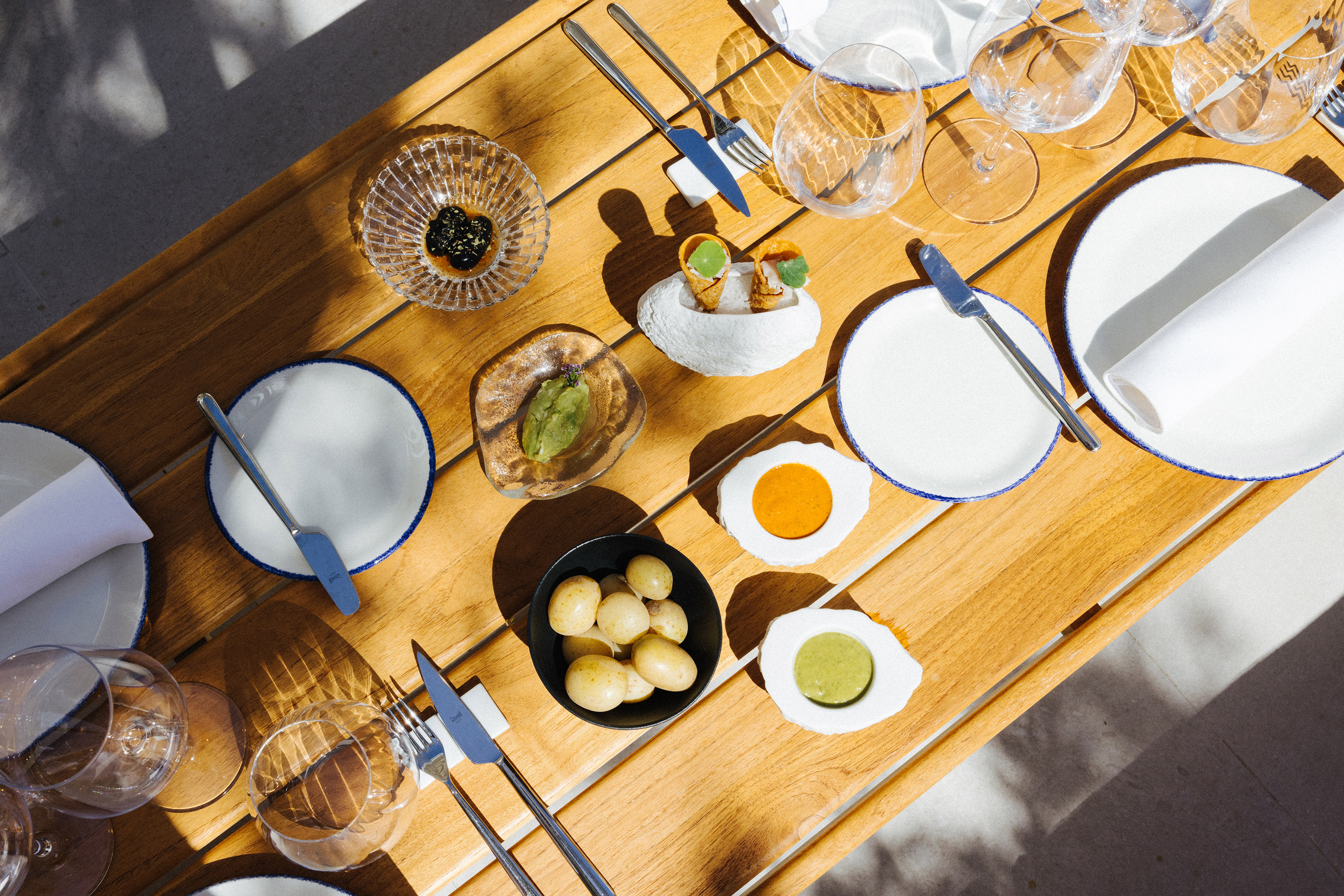 Gourmet appetizers, caviar, potatoes, sauces on a sunlit wooden table.