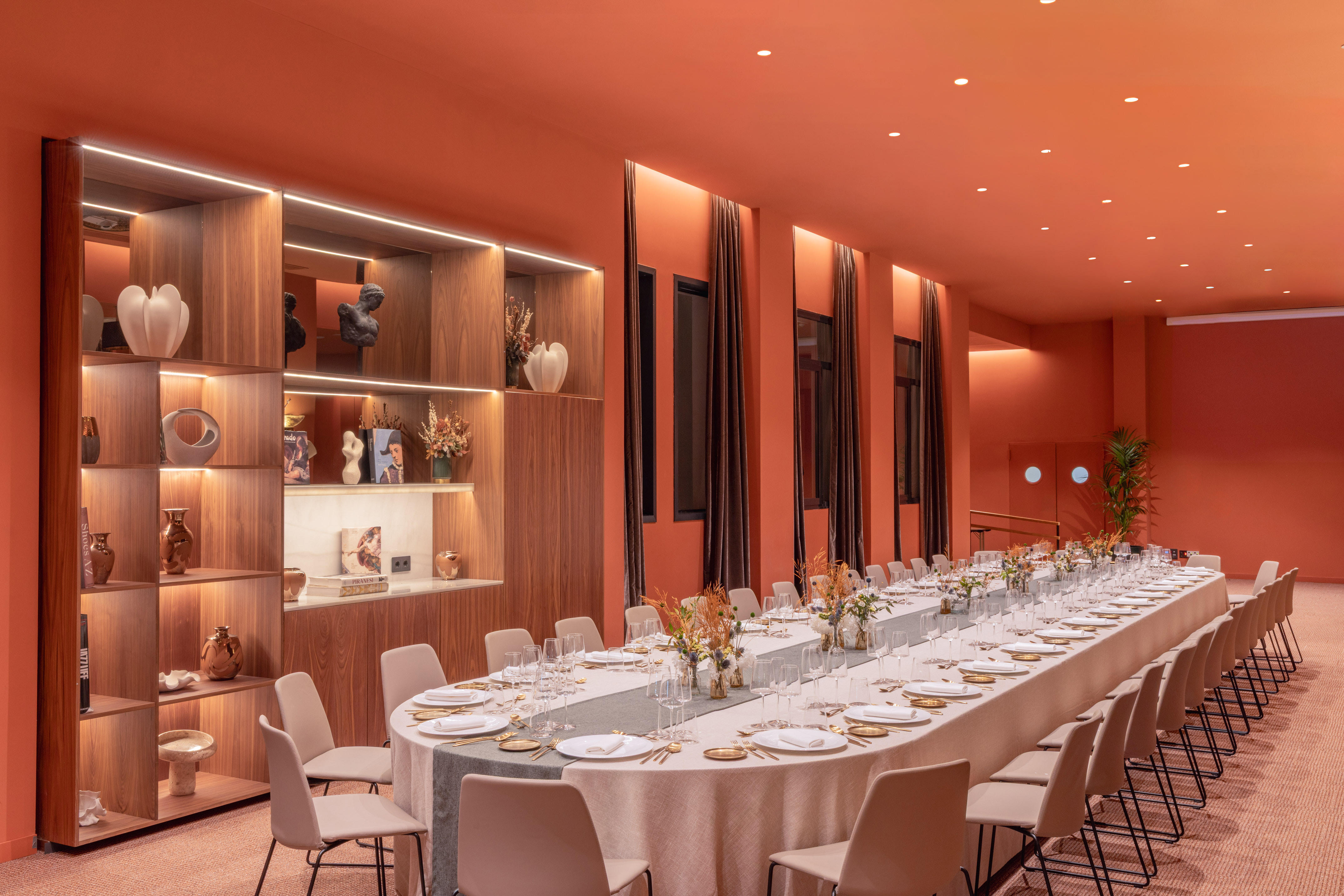 Orange modern dining room with long table set for event, decorative shelves.