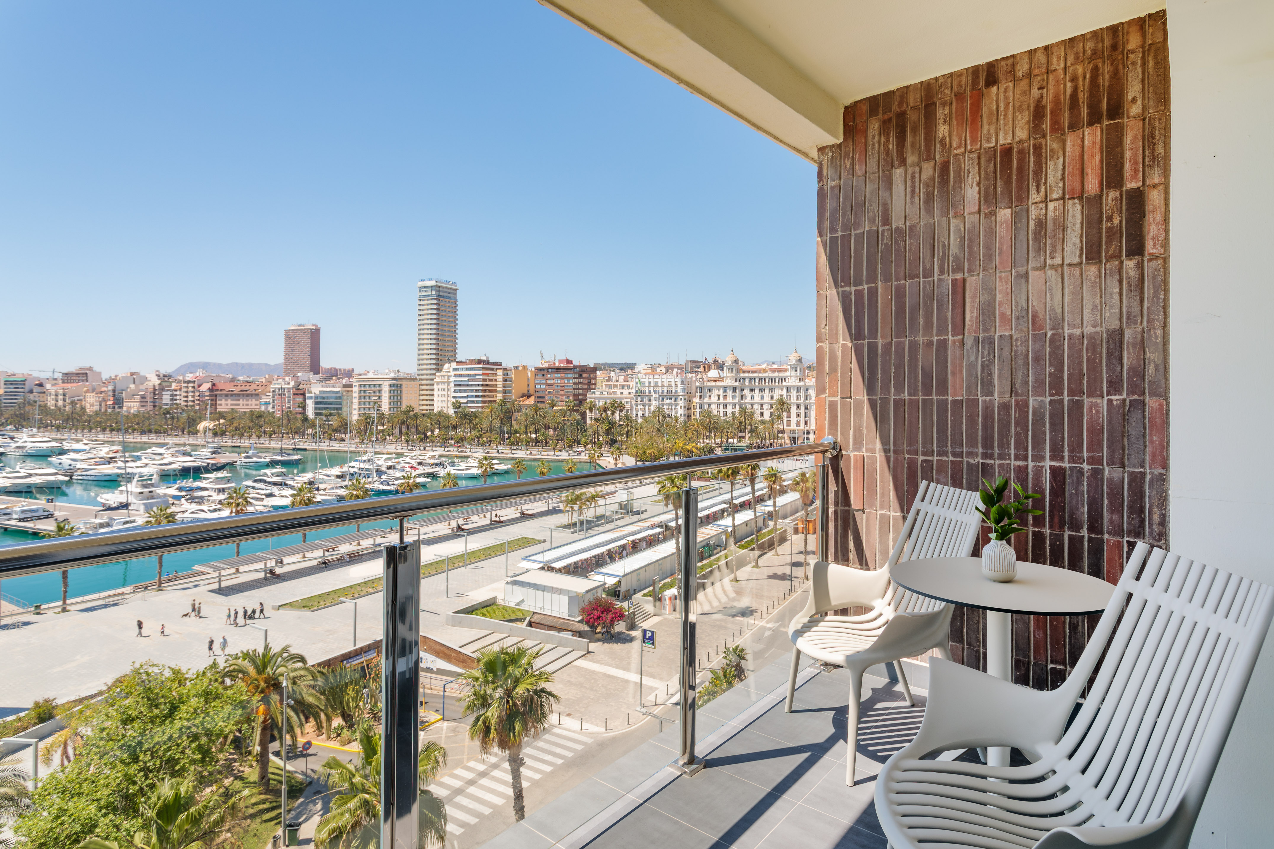 Sunny balcony overlooking marina with yachts, cityscape, and palm trees.