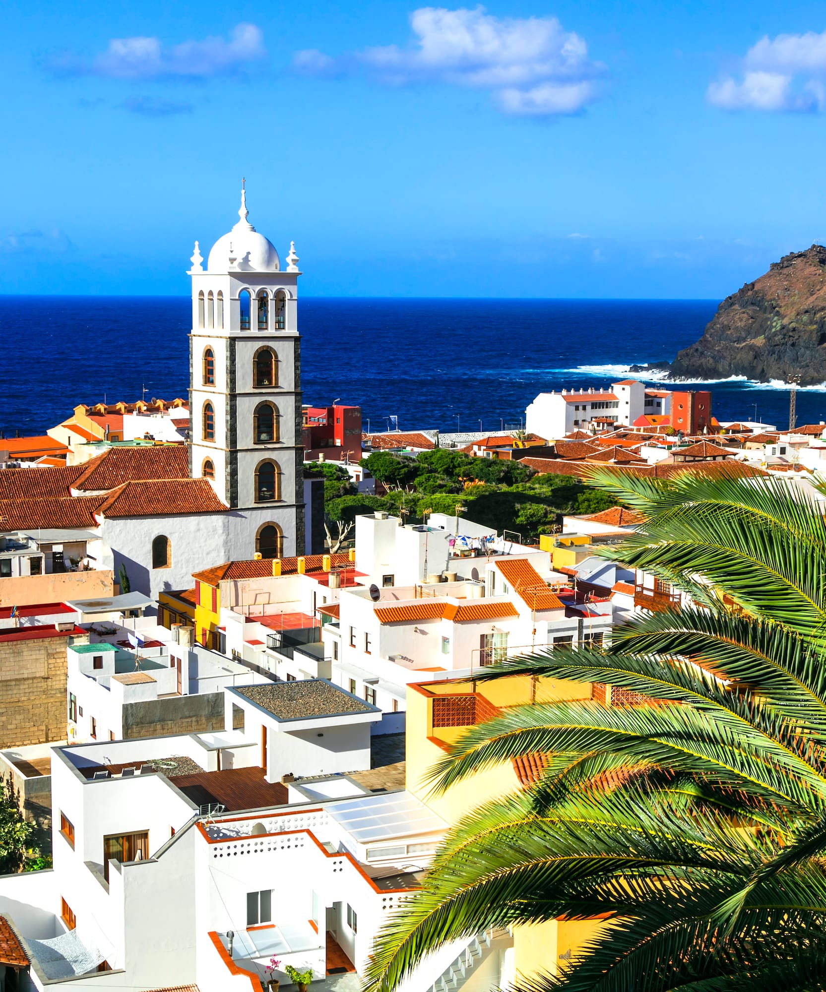 a white building with a tower and a palm tree next to the water