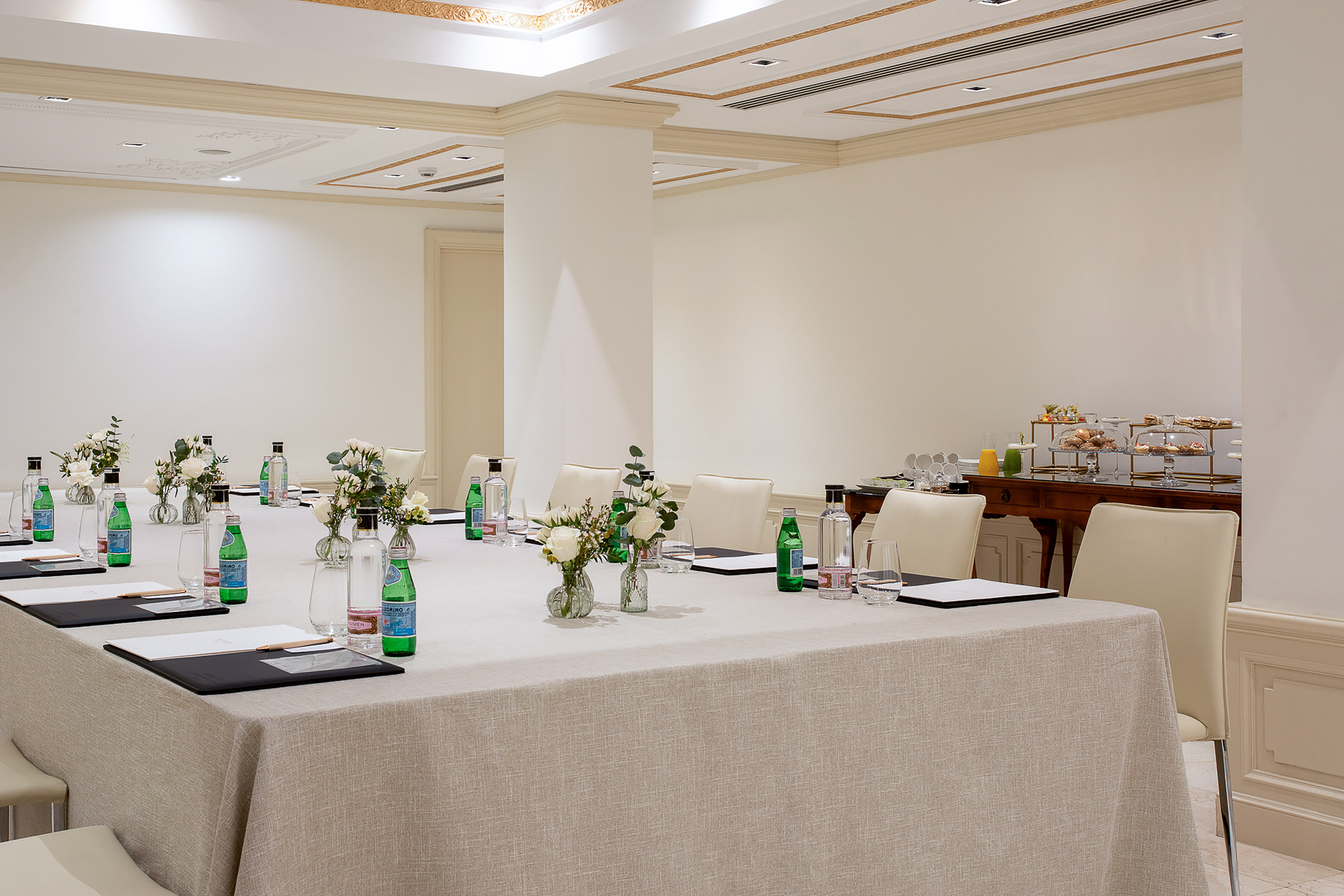 Professional meeting room with elegant table setup, water bottles, and buffet.