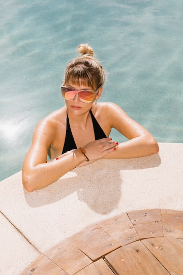 a woman in a garment and sunglasses leaning on a pool edge